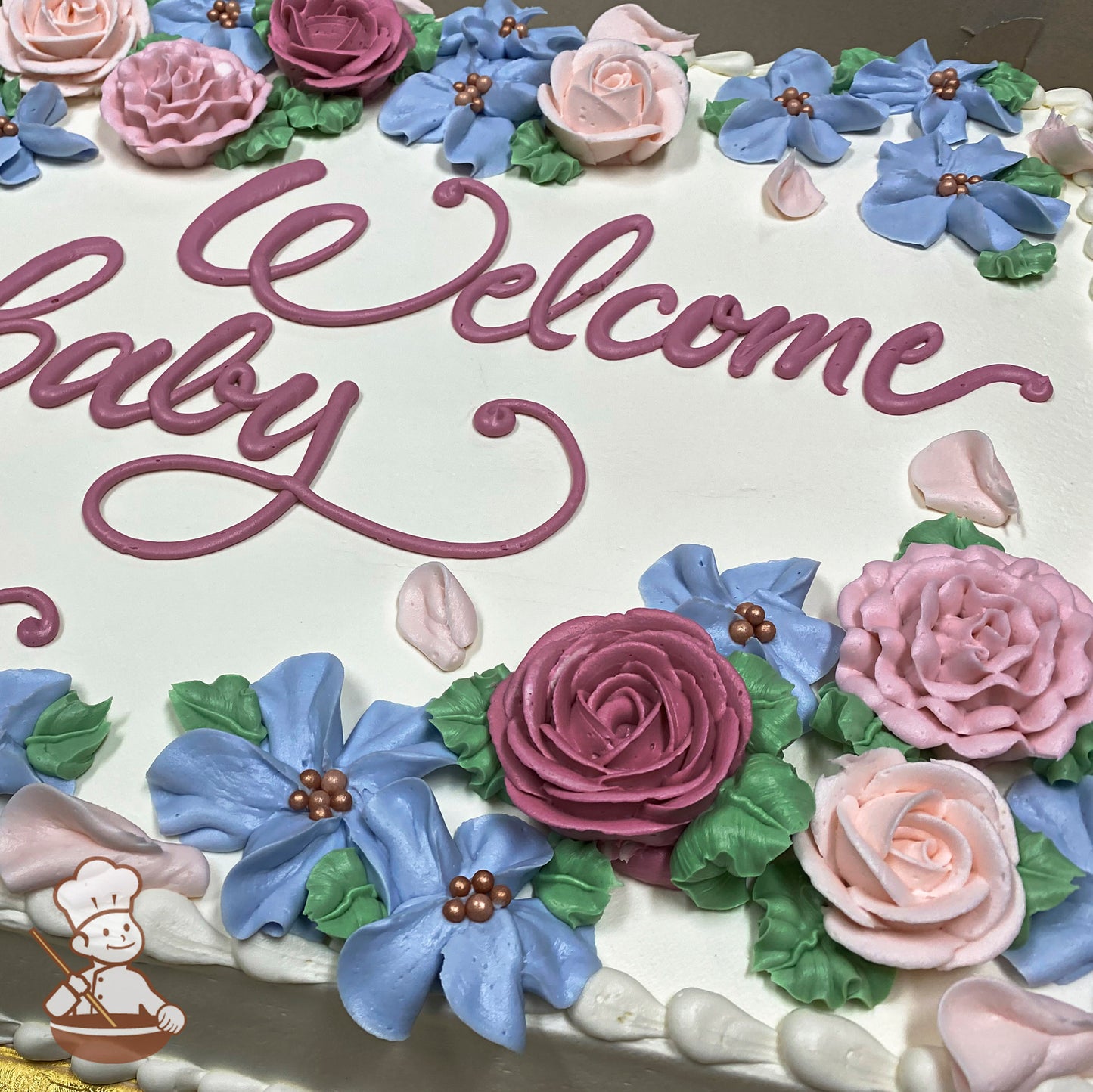 Sheet cake with white buttercream frosting, decorated with pink and blue buttercream flowers, green leaves, and pearl accents.