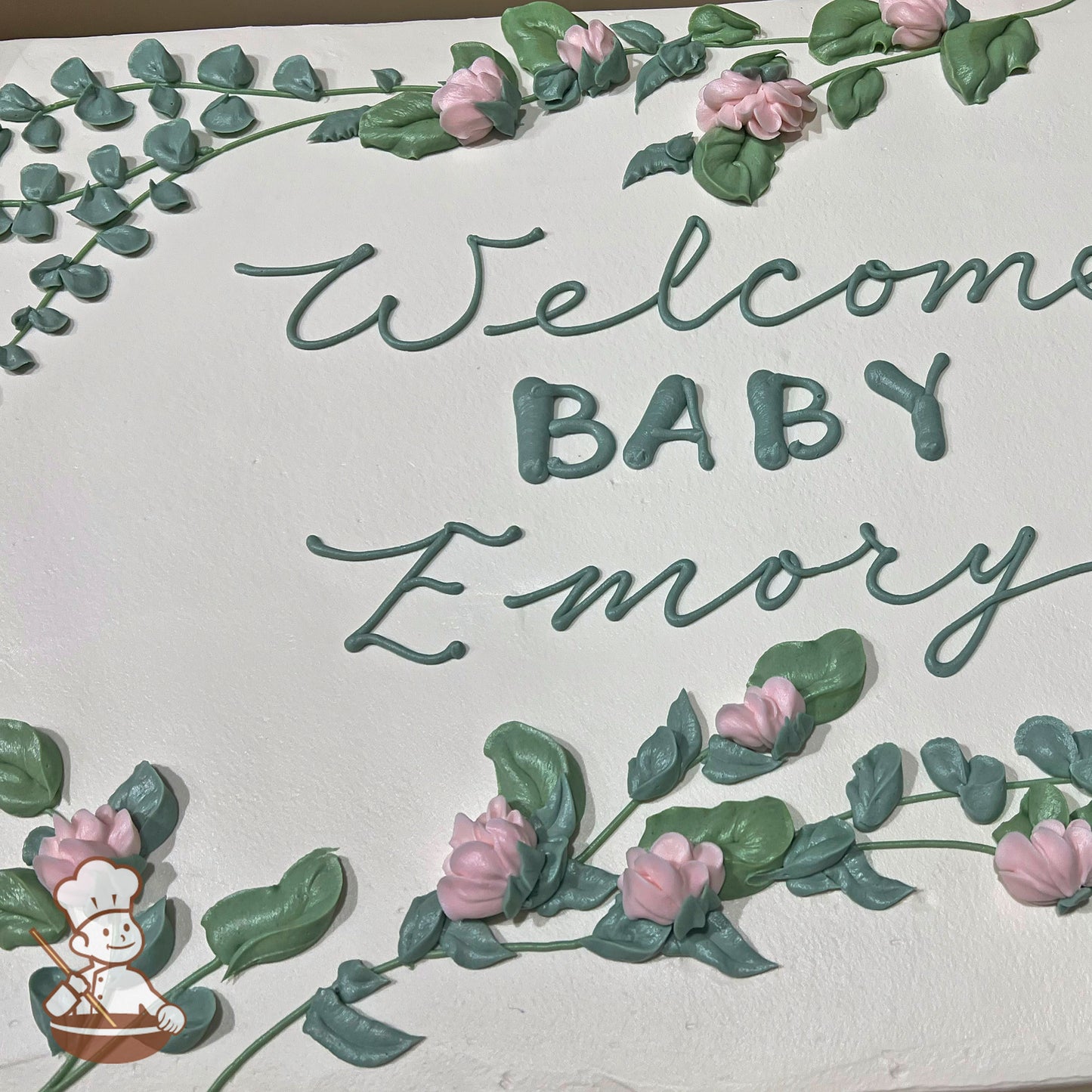 Sheet cake with buttercream decorations featuring pink baby bell flowers, sage green leaves, and vines arranged in a delicate floral design.