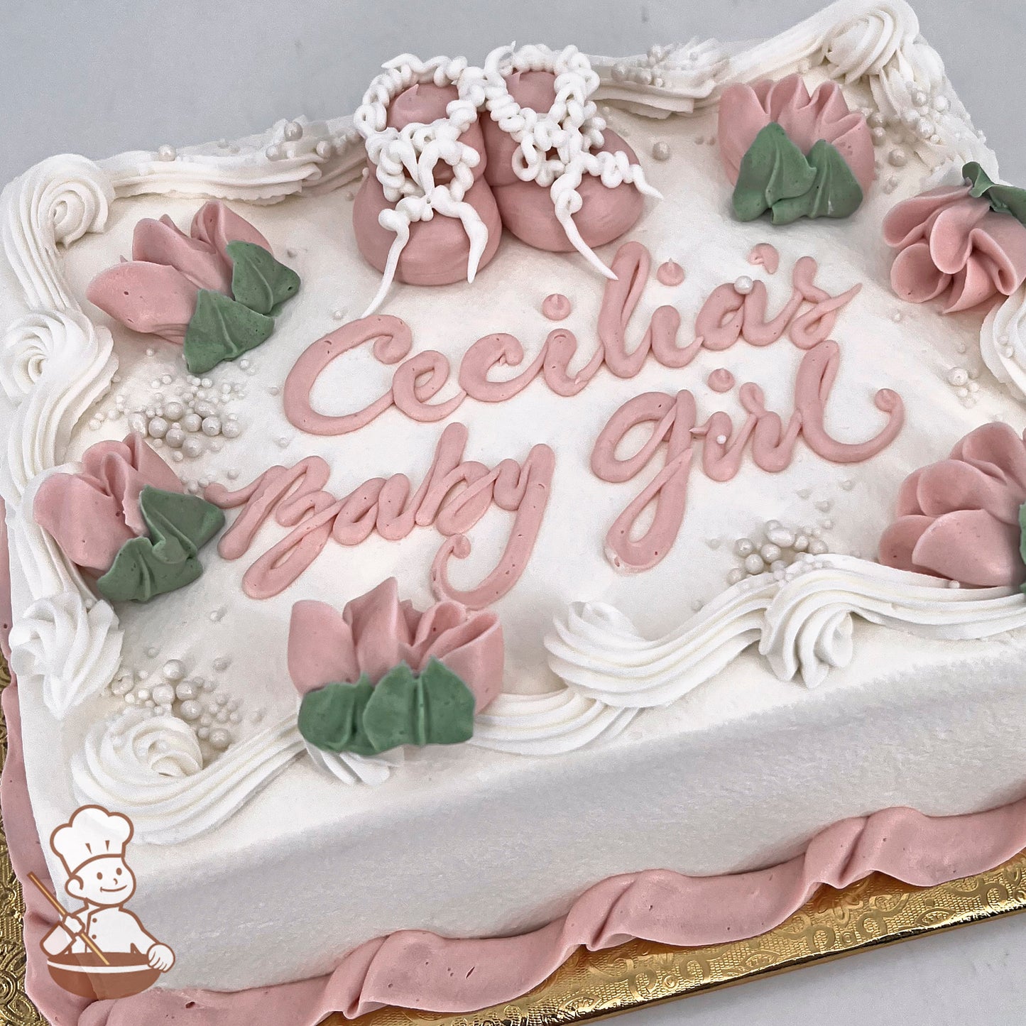 Sheet cake with pink buttercream baby booties, and bell flowers. Pastel pink and green floral decorations adorn the edges.