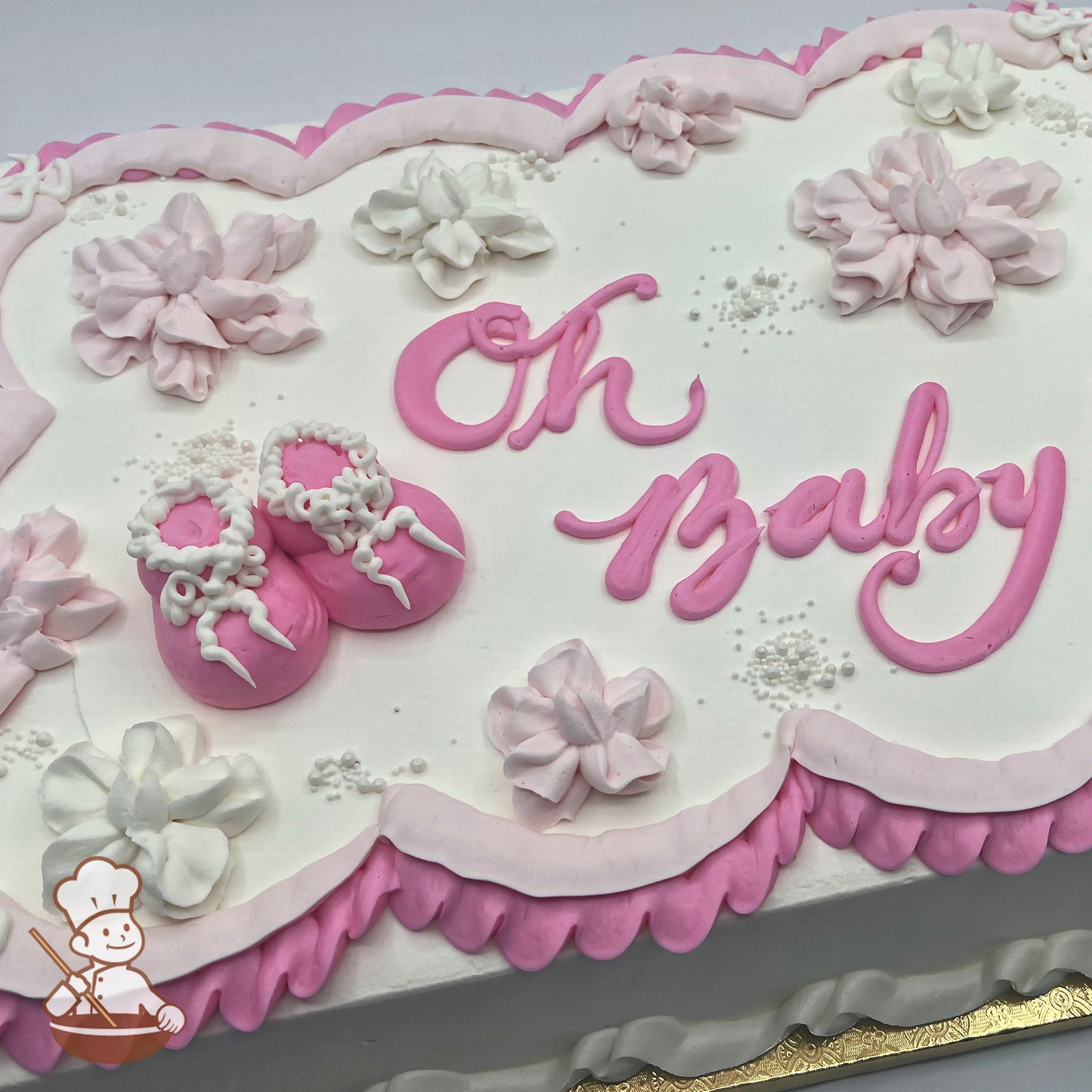 Sheet cake with pink and white buttercream decorations, including baby booties with ruffle trim, piped flowers, and scalloped borders.