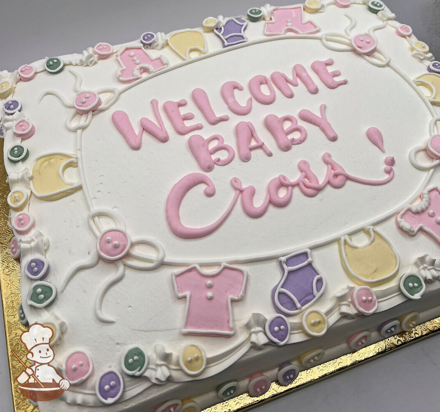 Sheet cake with pastel buttercream decorations, featuring baby clothes, buttons, bows, and a clothesline design around the edges.