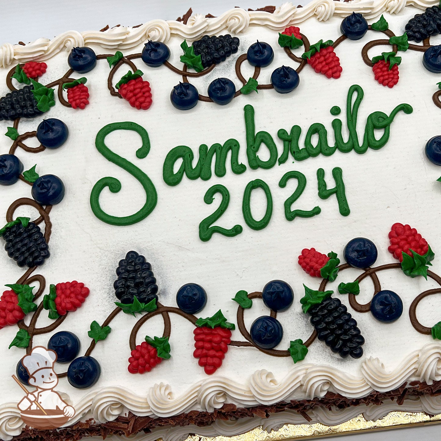 Sheet cake with white buttercream frosting, decorated with piped blueberries, blackberries, and raspberries on vines with green leaves, and a white swirled border.