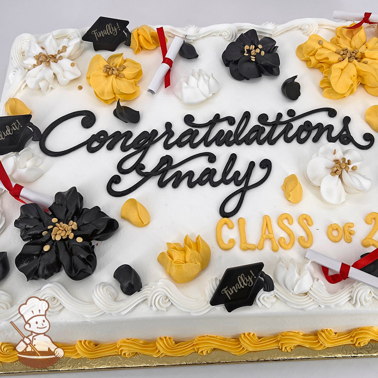 Sheet cake with white frosting, decorated with black, yellow, and white buttercream flowers, plastic graduation caps, diplomas, and yellow piping along the edges.