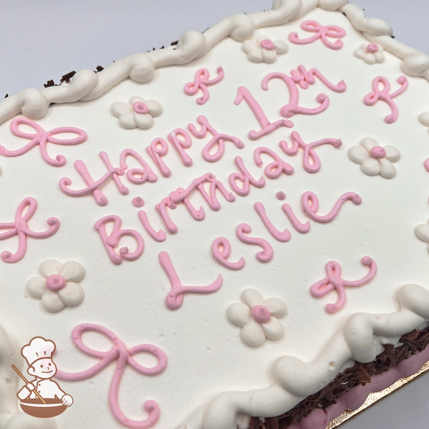 White sheet cake with pink buttercream bows, white buttercream daisies with pink centers, and a piped white border.