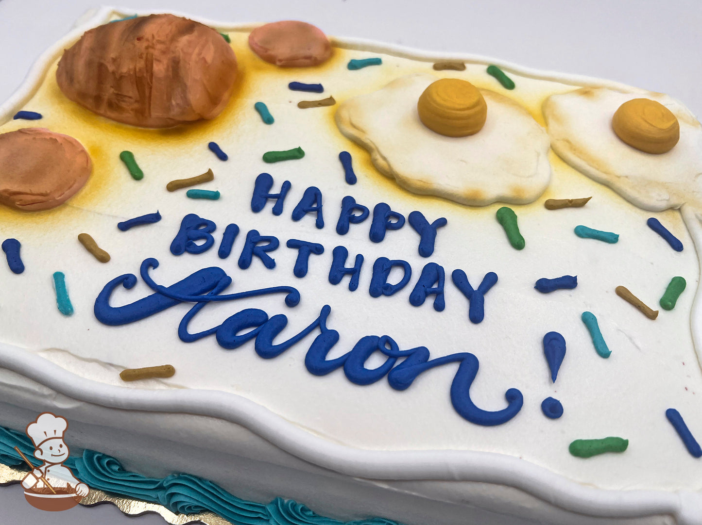 Sheet cake with buttercream decorations featuring fried eggs, ham, hand-piped colorful sprinkles, and a blue border design.