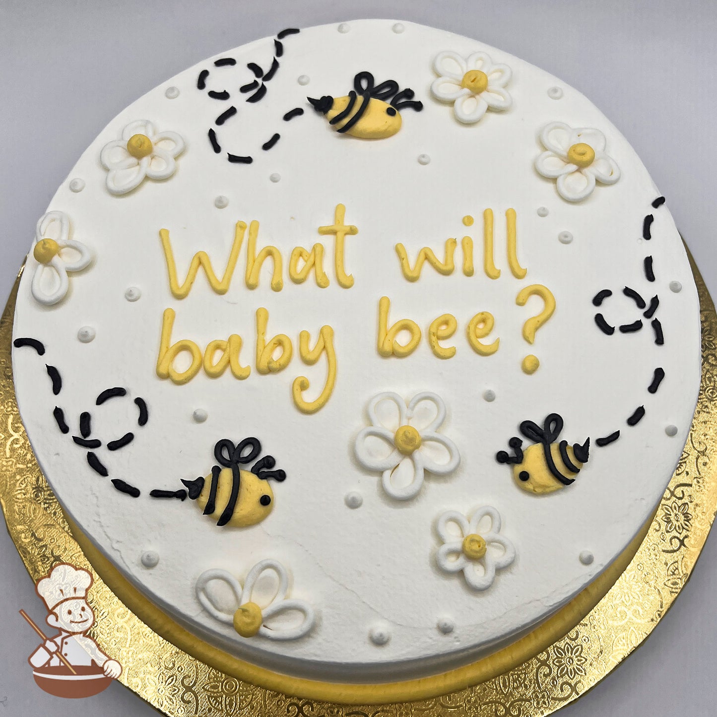 Round cake with white icing, decorated with yellow and black bees, outlined white daisies with yellow centers, and dotted flight paths.