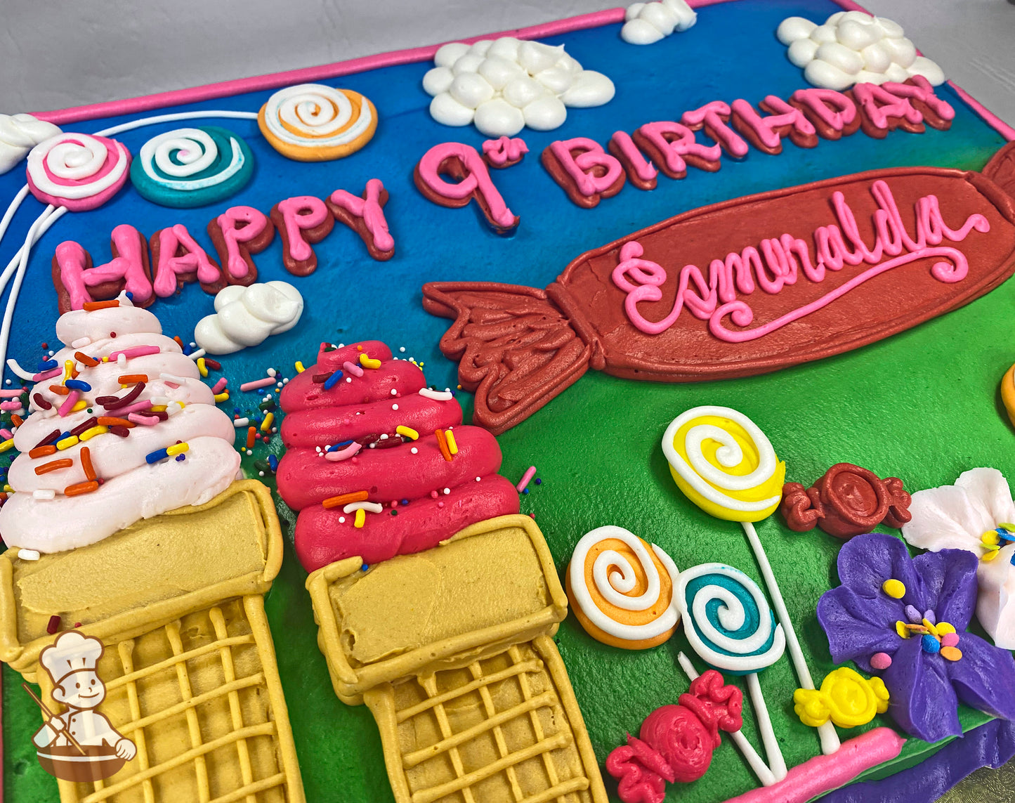 Sheet cake with buttercream decorations of pink ice cream cones, colorful lollipops, candy pieces, fluffy clouds, and purple and pink flowers.
