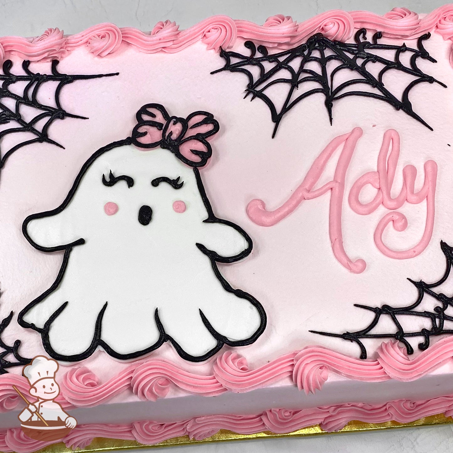 Sheet cake with pink buttercream border, featuring a cute ghost with a pink bow and black spider webs.
