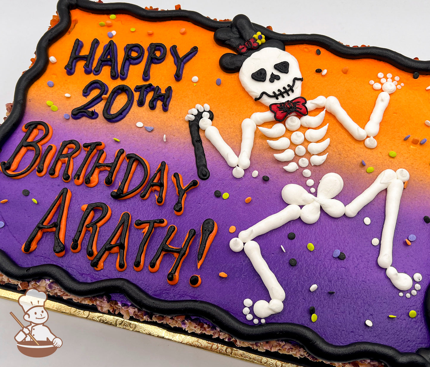Sheet cake with orange and purple gradient, featuring a hand-piped skeleton wearing a top hat and bow tie, surrounded by colorful sprinkles.