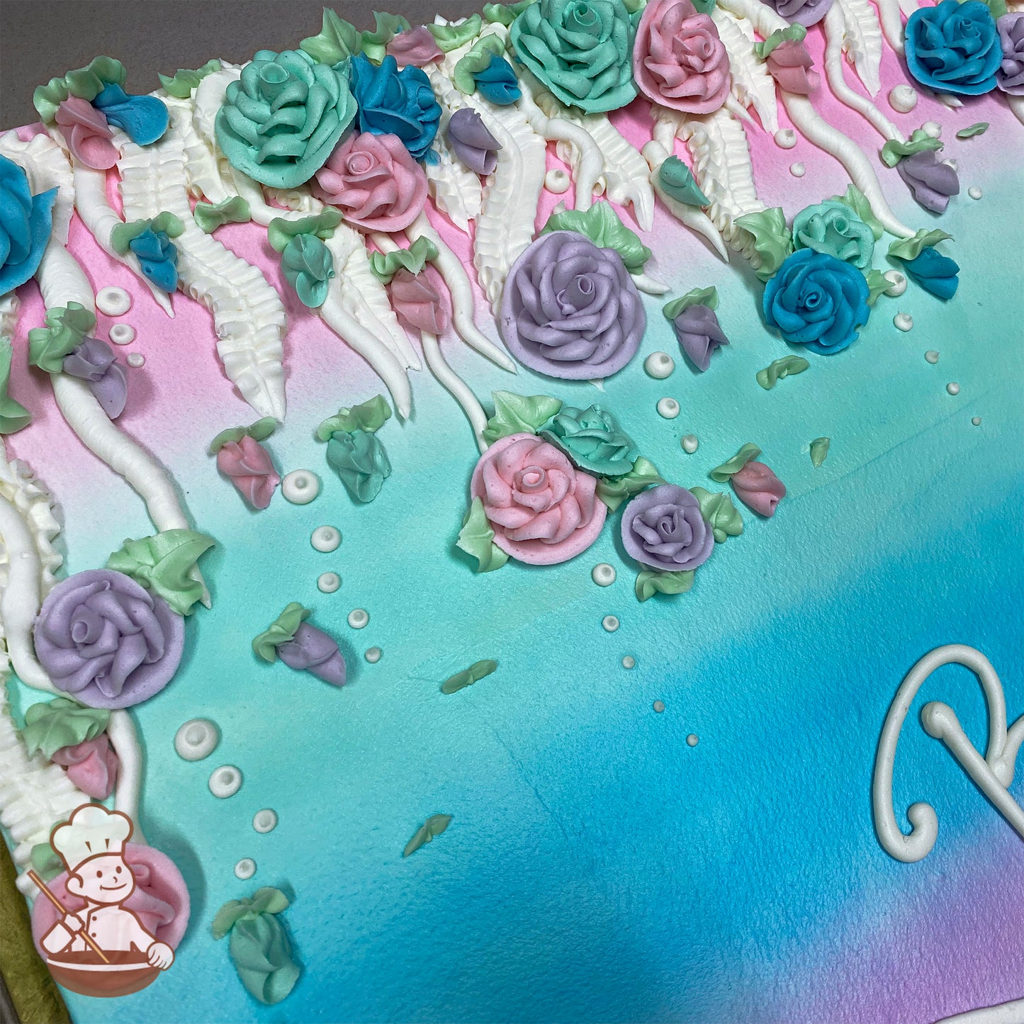 Sheet cake with pastel ombre frosting, decorated with hand-piped buttercream roses in pink, purple, blue, and teal draped on vines with white accents.