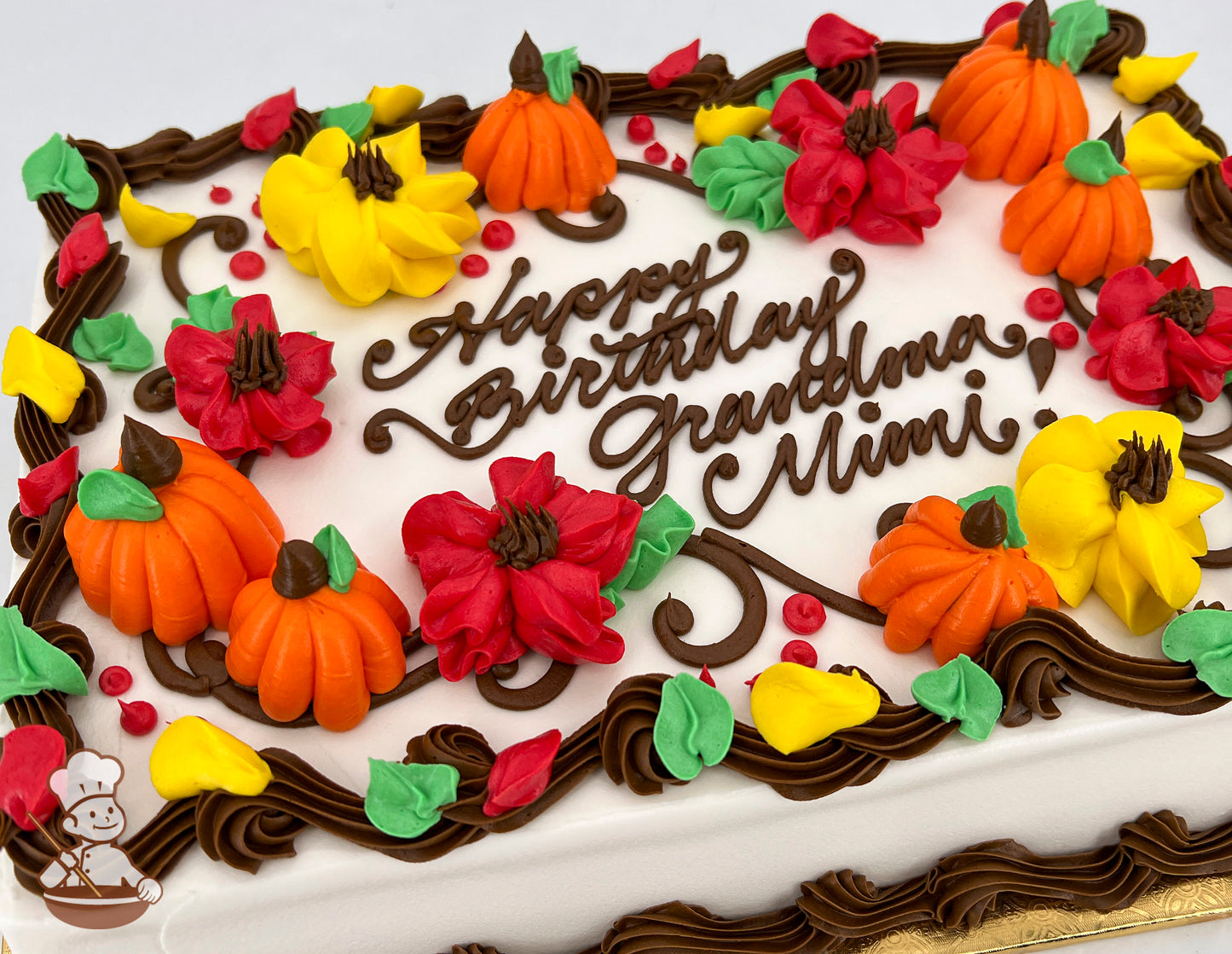 Sheet cake with buttercream decorations of orange pumpkins, red and yellow blossoms, and green leaves, bordered by brown swirls.