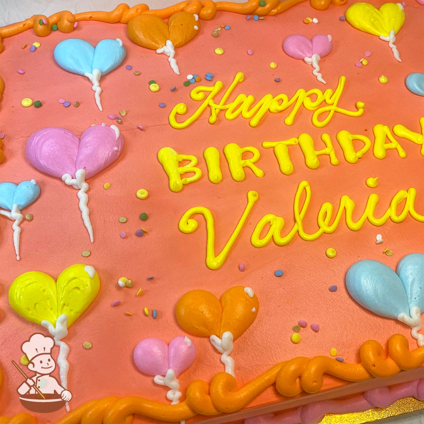 Sheet cake with a peach-colored icing base, decorated with hand-piped heart-shaped balloons in pink, blue, yellow, and orange, and scattered colorful sprinkles.