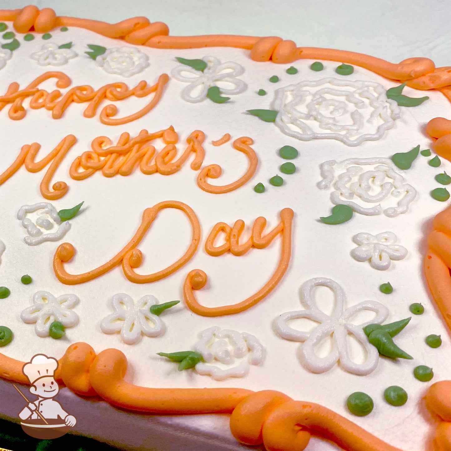 Sheet cake with orange buttercream border, white piped flowers, and green leaves.