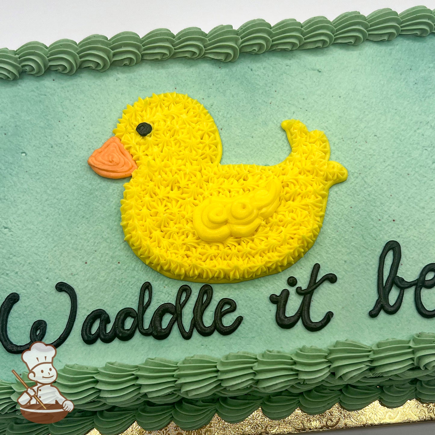 Sheet cake with light green frosting, a yellow hand-piped buttercream duck with an orange beak, and a green piped border.