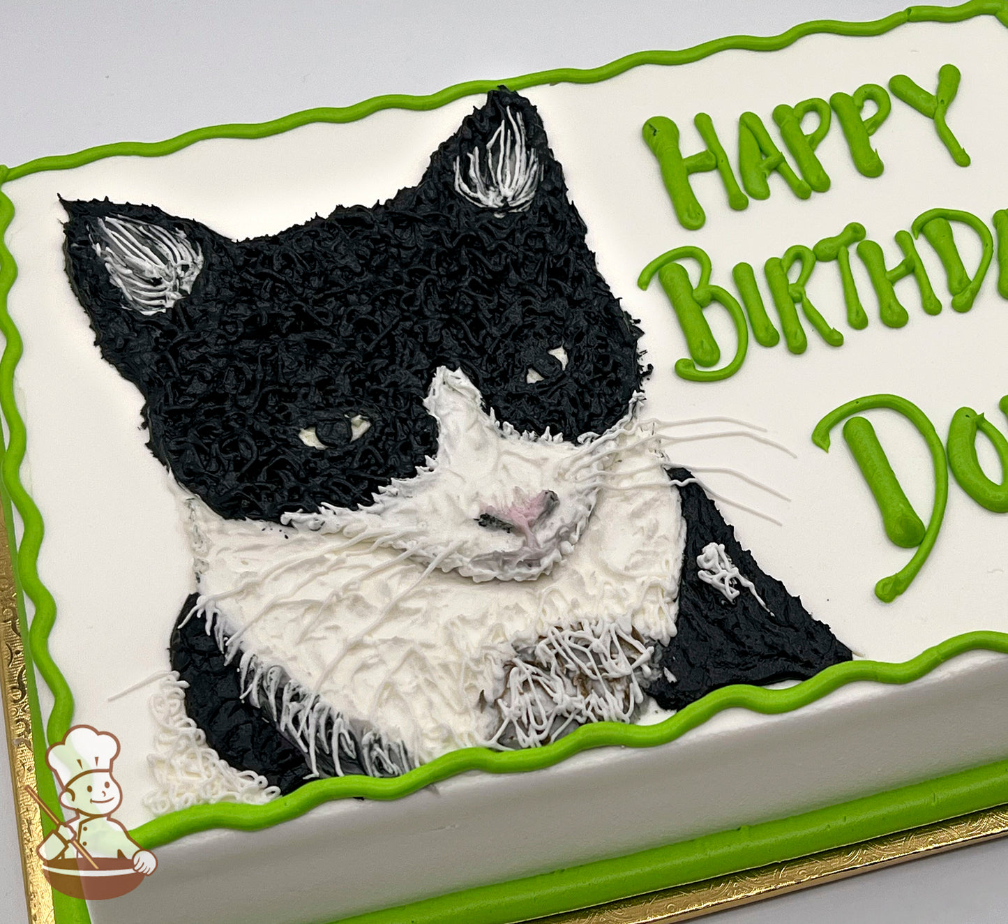 Sheet cake with a black-and-white cat design in icing, featuring detailed fur texture. Green piped border and accents.