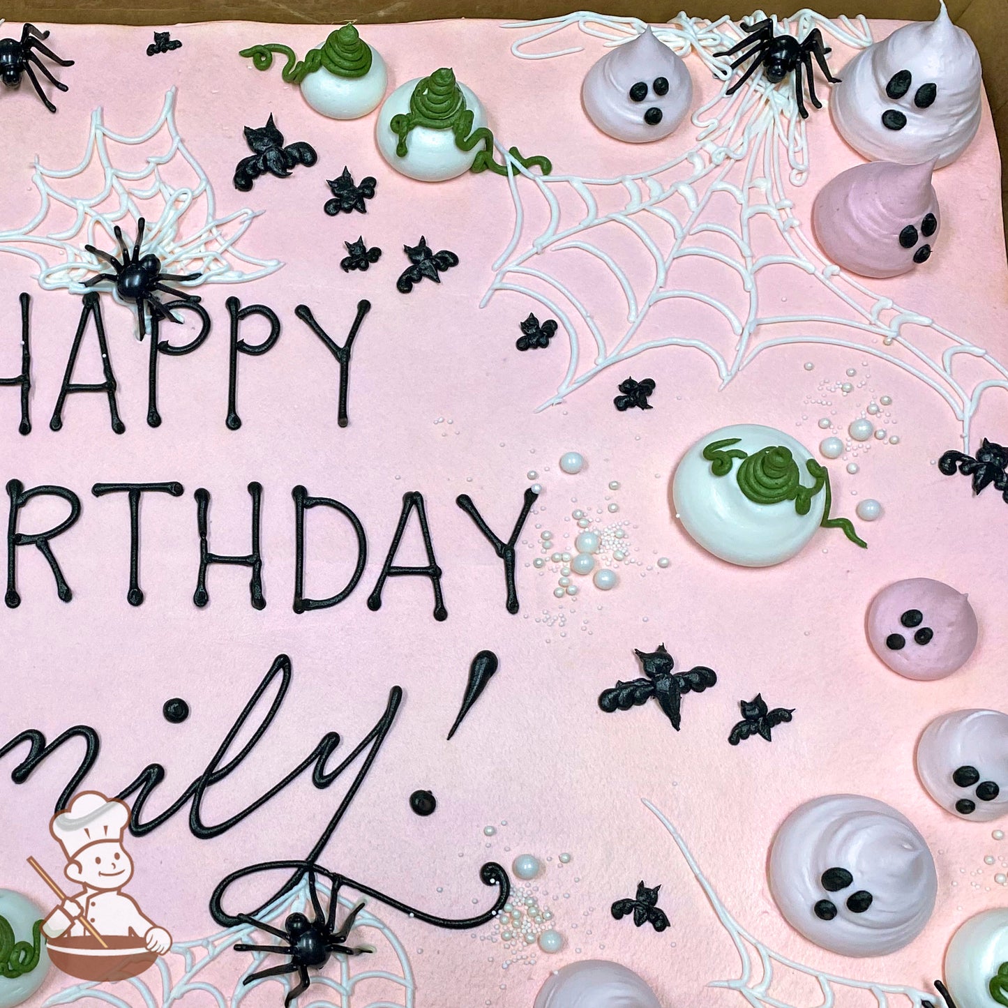 Pink sheet cake with buttercream ghosts, black bats, white spider webs, plastic spiders, and scattered white sugar pearls for decoration.