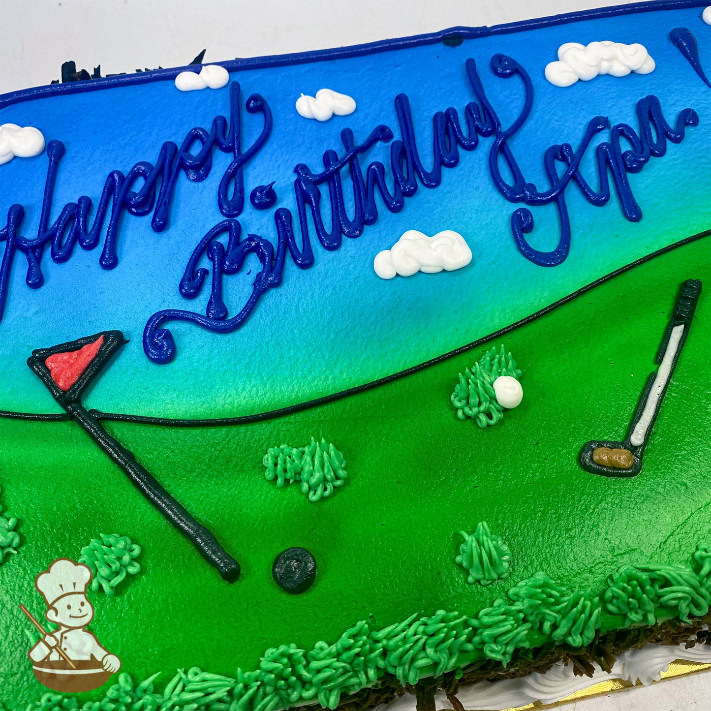 Sheet cake with buttercream decorations of a golf course, featuring a golf club, flag, and ball on green grass under a blue sky with clouds.