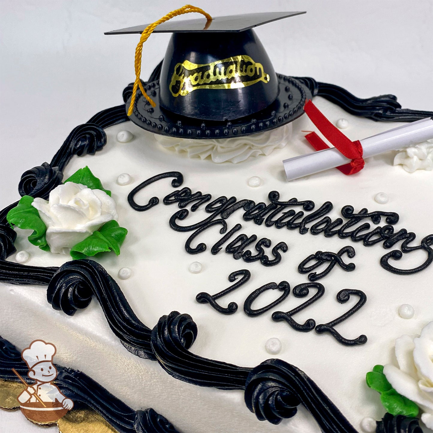 Sheet cake with white frosting, black piped borders, white buttercream roses with green leaves, plastic graduation cap toy, and paper diploma.