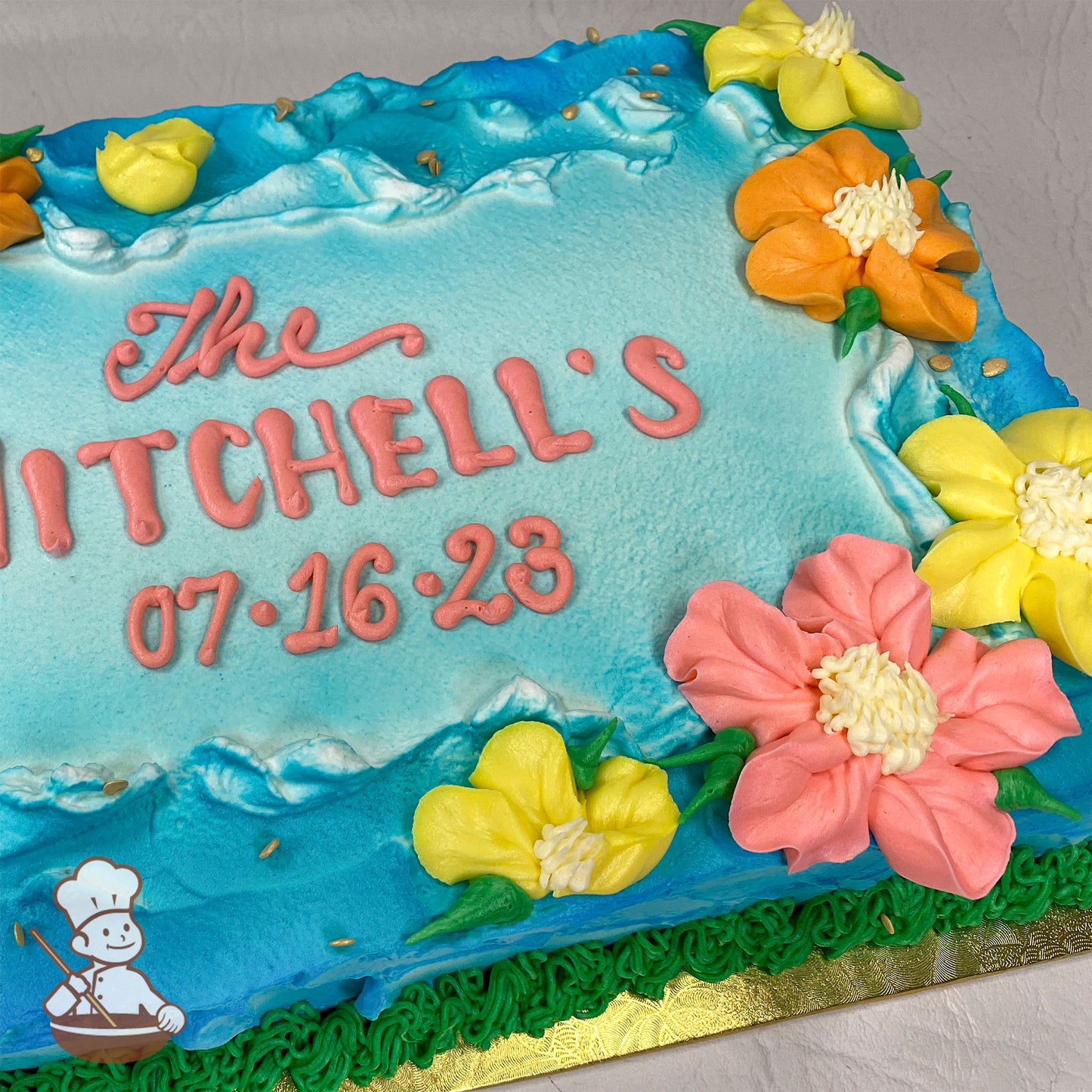 Sheet cake with a blue ocean-like frosting background, bordered by yellow, orange, and pink flowers, with green piping at the base.