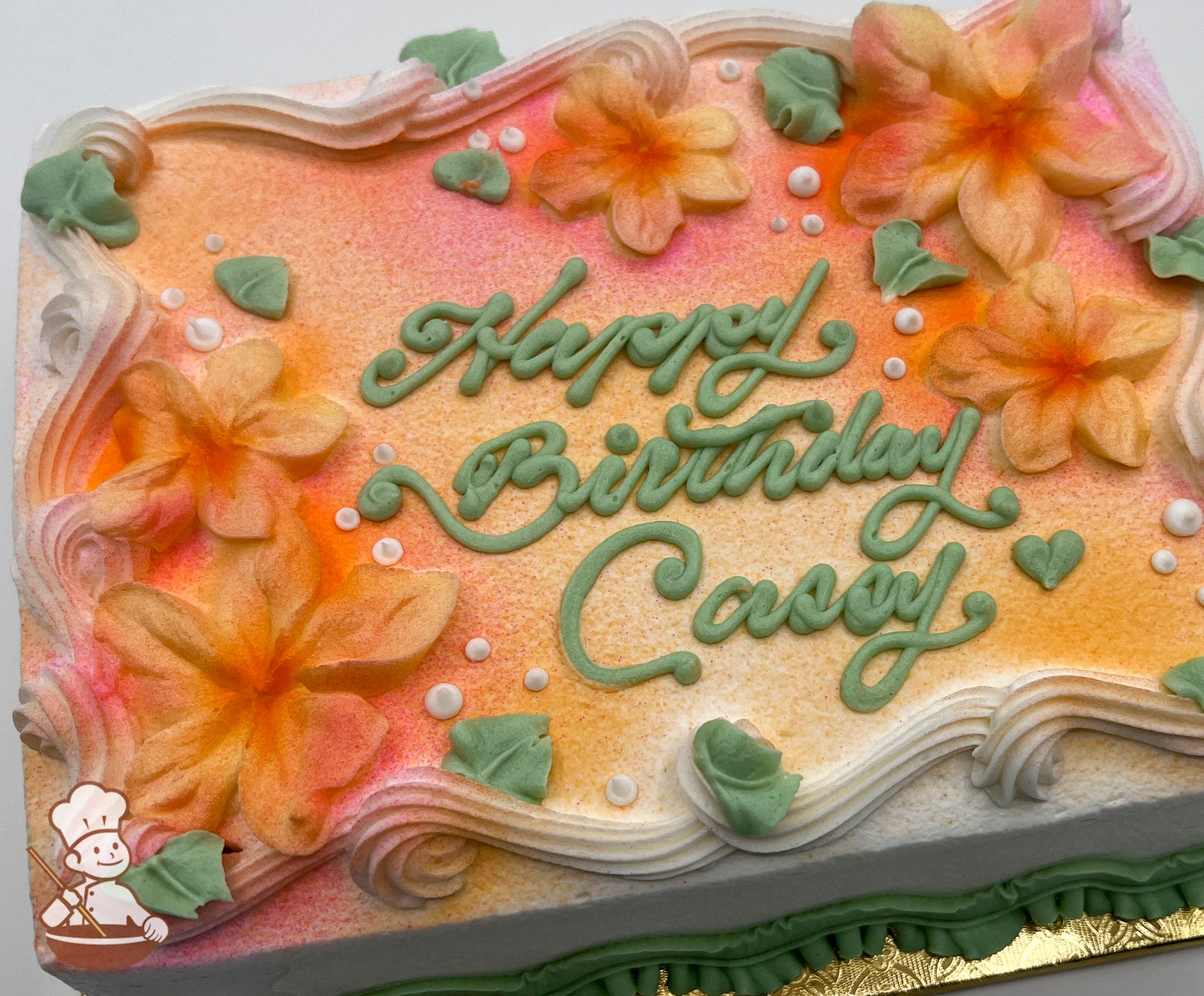 Sheet cake with orange and pink airbrushed flowers, decorated with plumeria flowers, green leaves, white dots, and piped swirl trims.