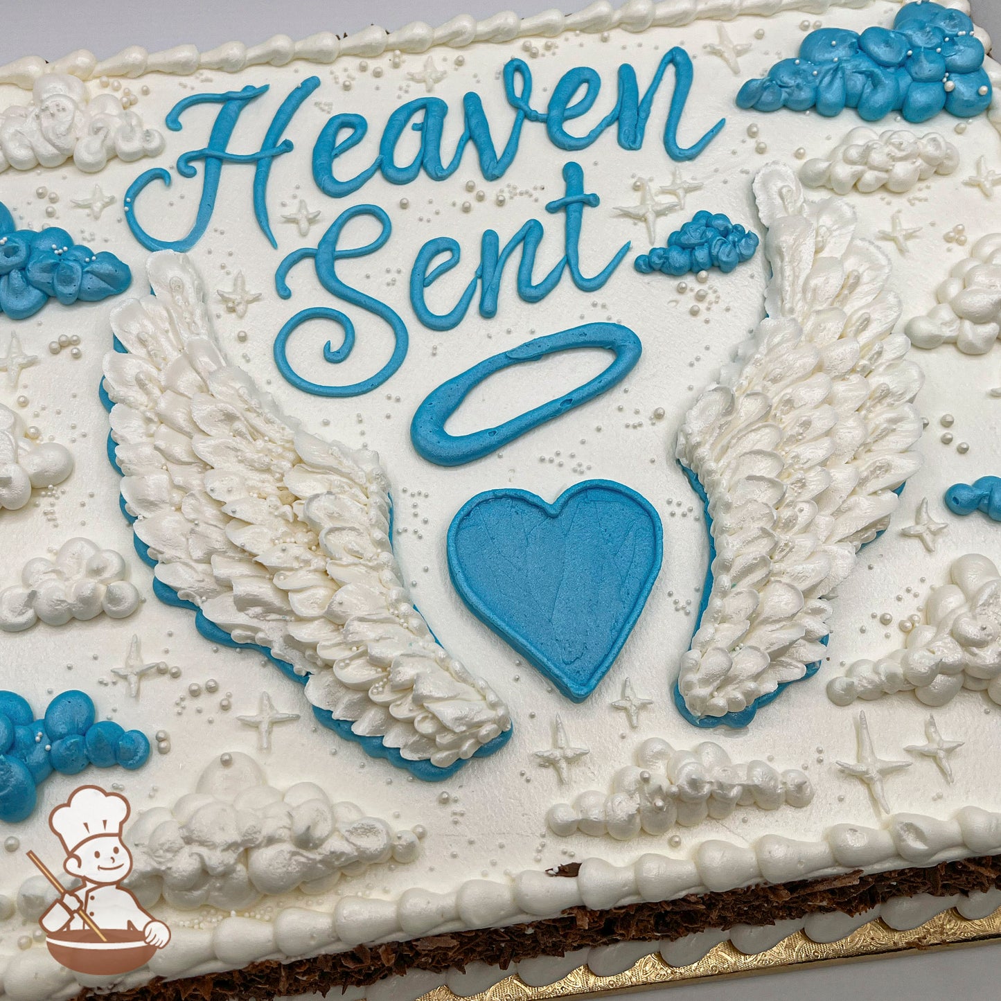 Sheet cake with white frosting, decorated with angel wings, a blue heart, a halo, clouds, stars, and pearl accents.