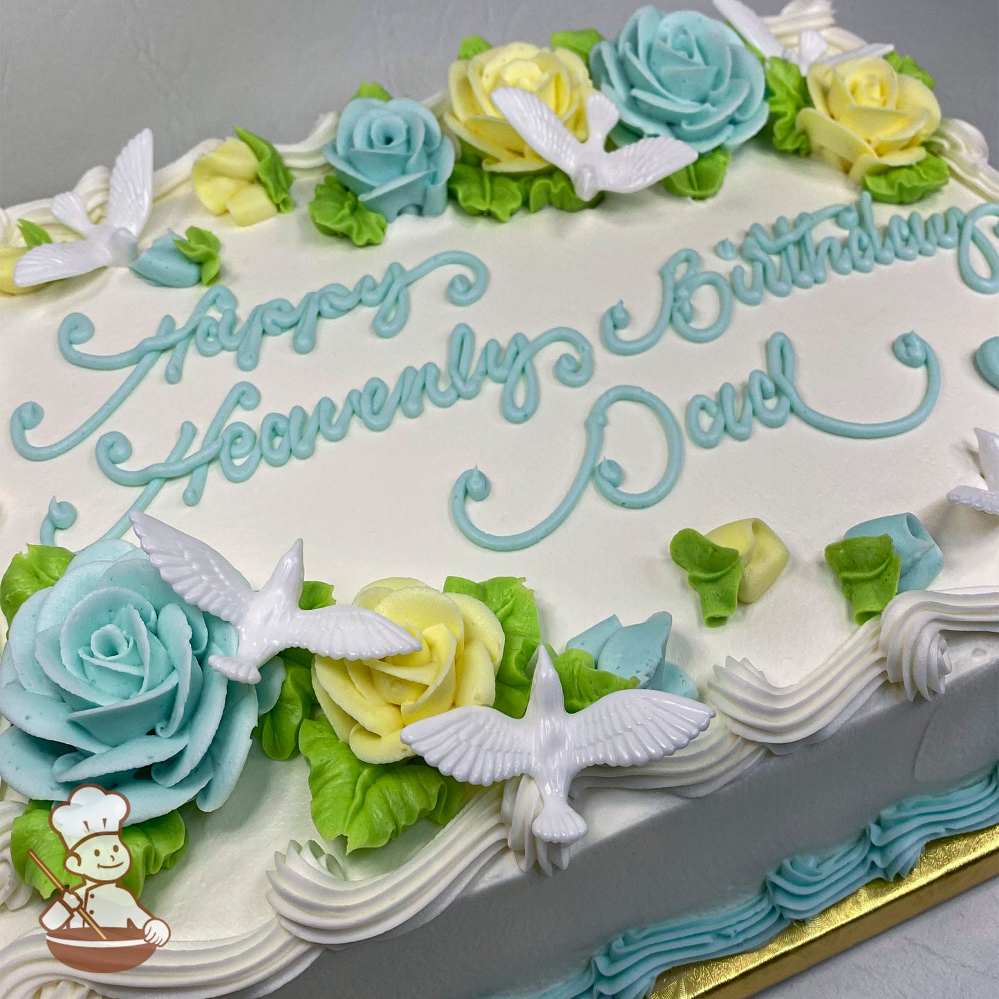 Sheet cake with white frosting, decorated with pastel blue and yellow buttercream roses, green leaves, and white plastic dove figurines.