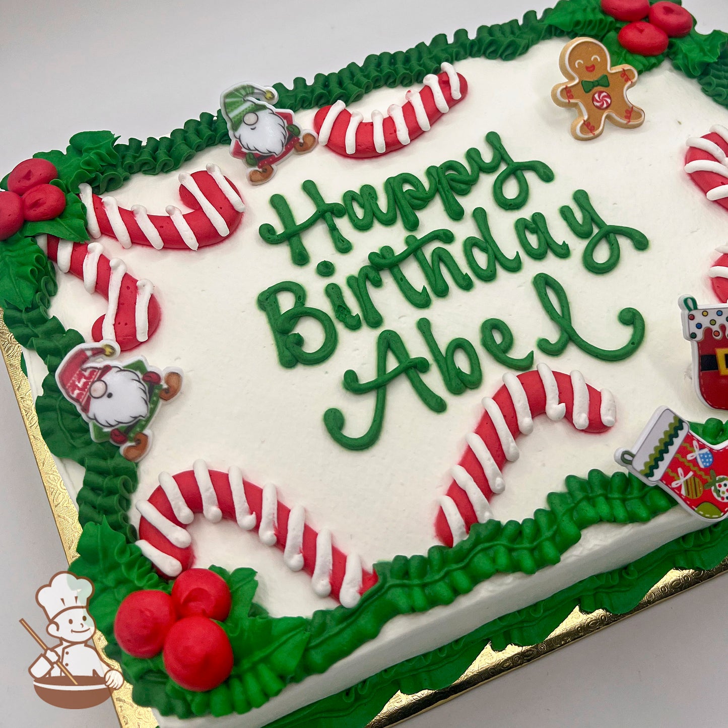 Sheet cake with buttercream candy canes, green leaves, red berries, plastic gnomes, gingerbread man, and Christmas stocking decorations.