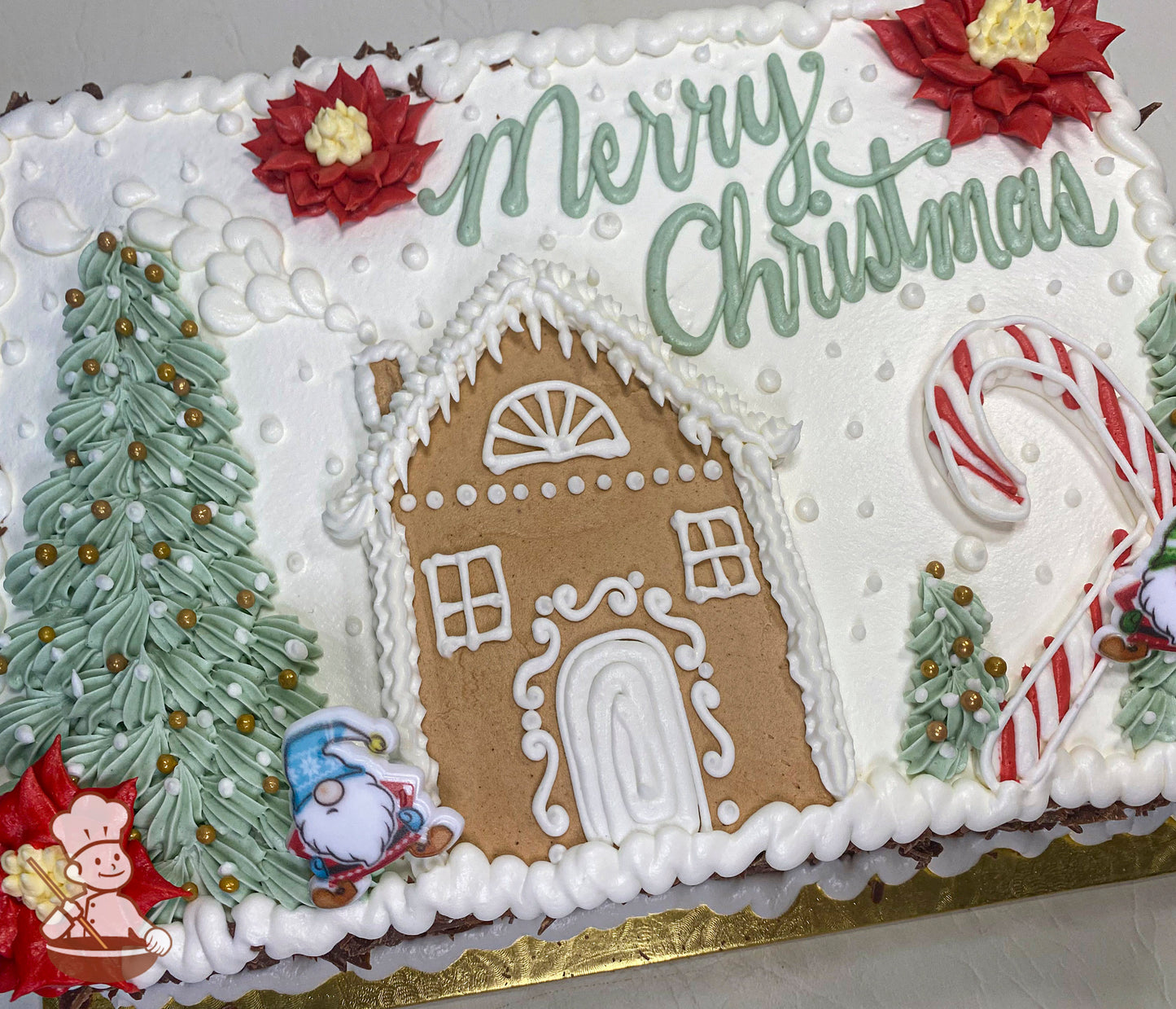 Sheet cake with white frosting, decorated with a gingerbread house, green Christmas trees, red poinsettias, candy canes, and snow accents.