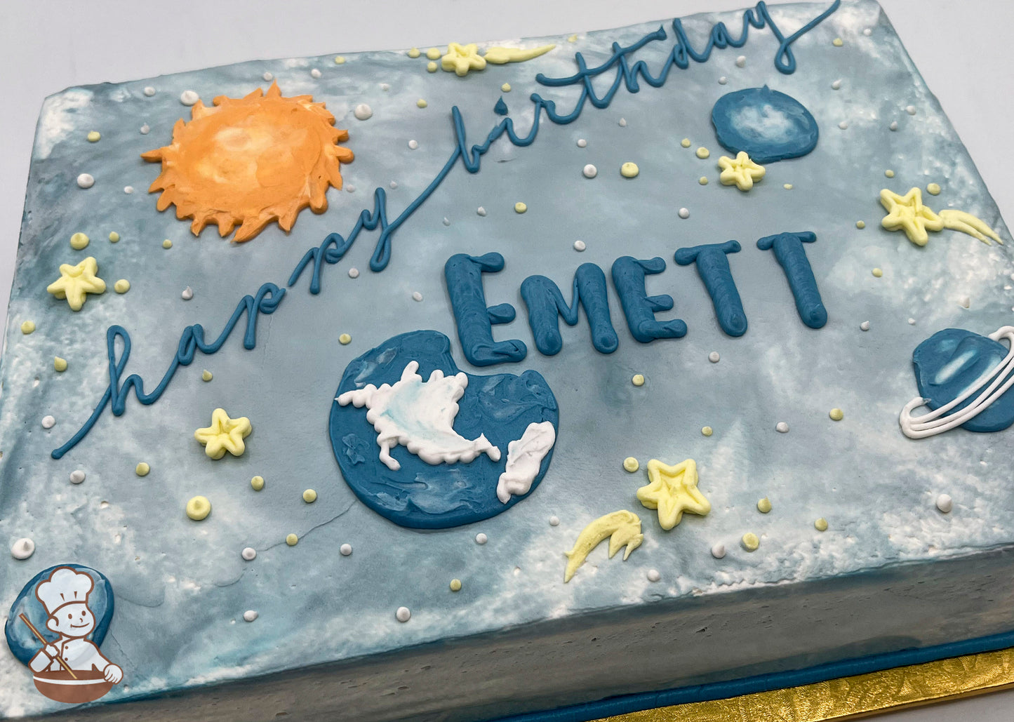 Sheet cake with colored icing, decorated with a sun, planets, stars, and a ringed planet. White and yellow dots resemble stars.
