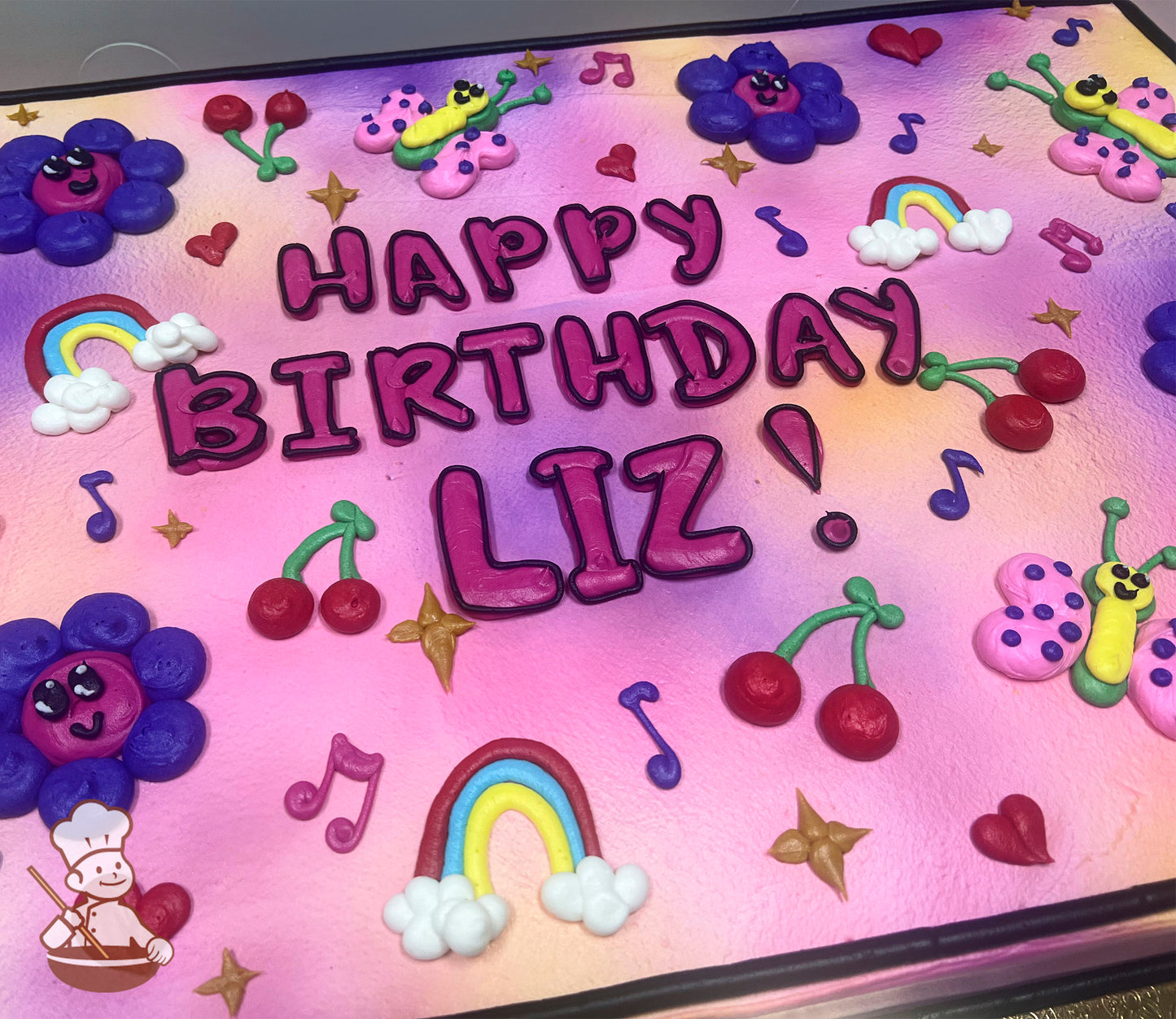 Colorful sheet cake with a pink and purple gradient background, decorated with buttercream flowers, rainbows, music notes, stars, cherries, butterflies, and hearts.