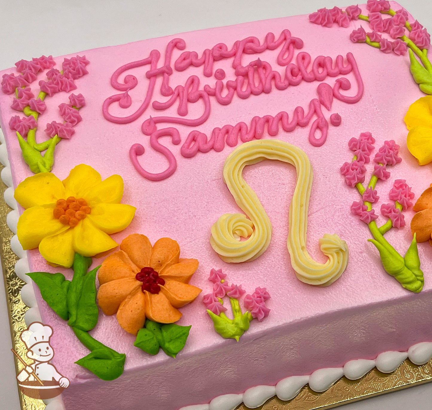 Pink sheet cake with buttercream Leo zodiac sign, yellow and orange flowers, pink floral accents, and white frosting border.