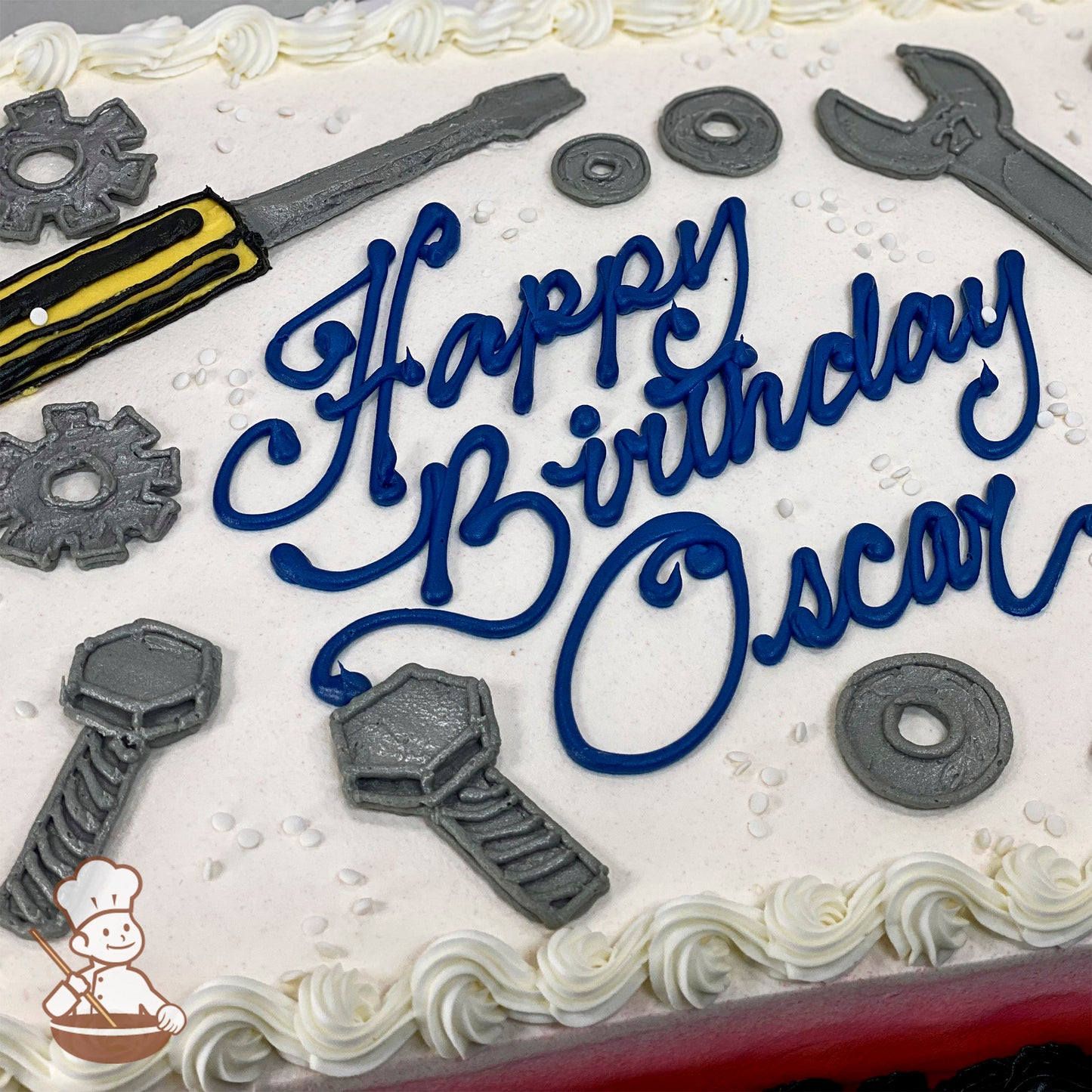 Sheet cake with white frosting, decorated with buttercream tools including a wrench, screwdriver, bolts, washers, and gears, with piped white border.