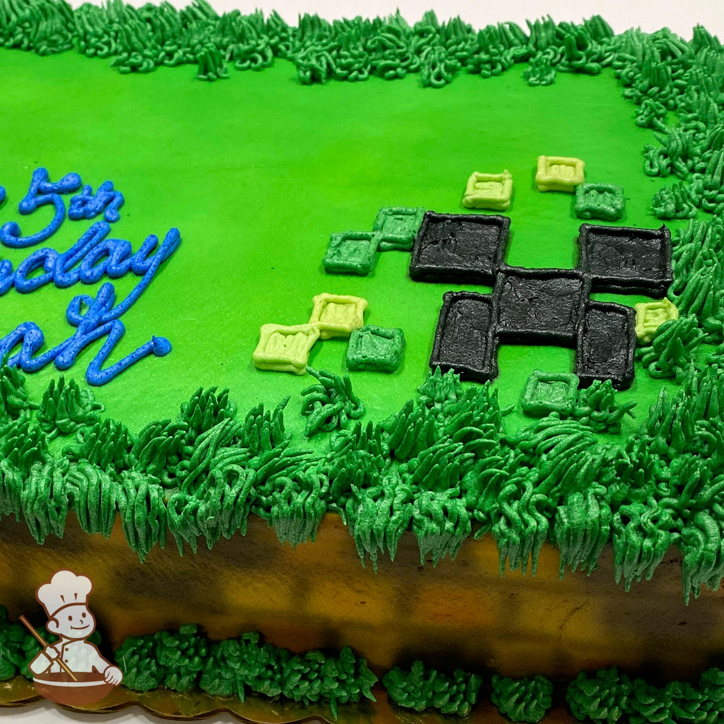 Sheet cake with green frosting, grass-like piping along the edges, and a black and green pixelated Creeper face design resembling Minecraft blocks.