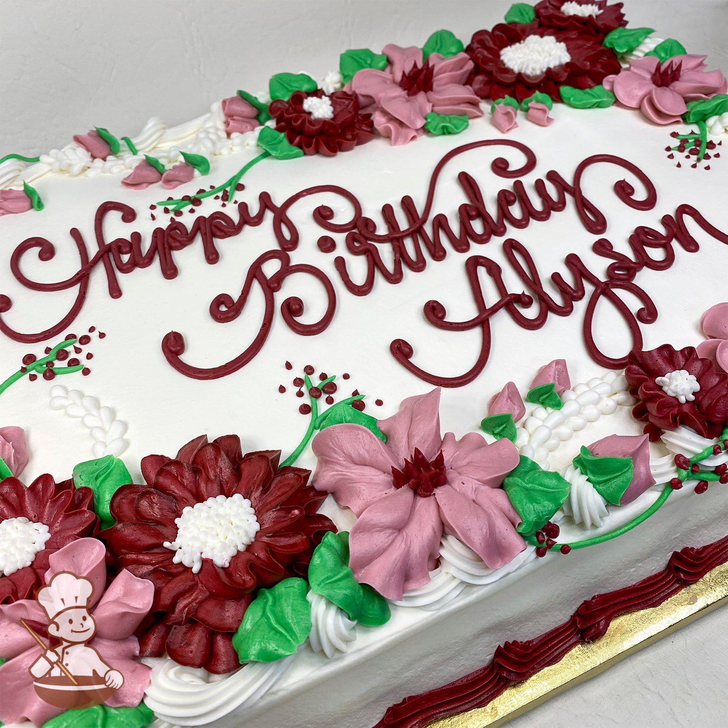 White sheet cake with buttercream decorations featuring burgundy mums, pink blossom flowers, green leaves, white piped accents, and a burgundy border.