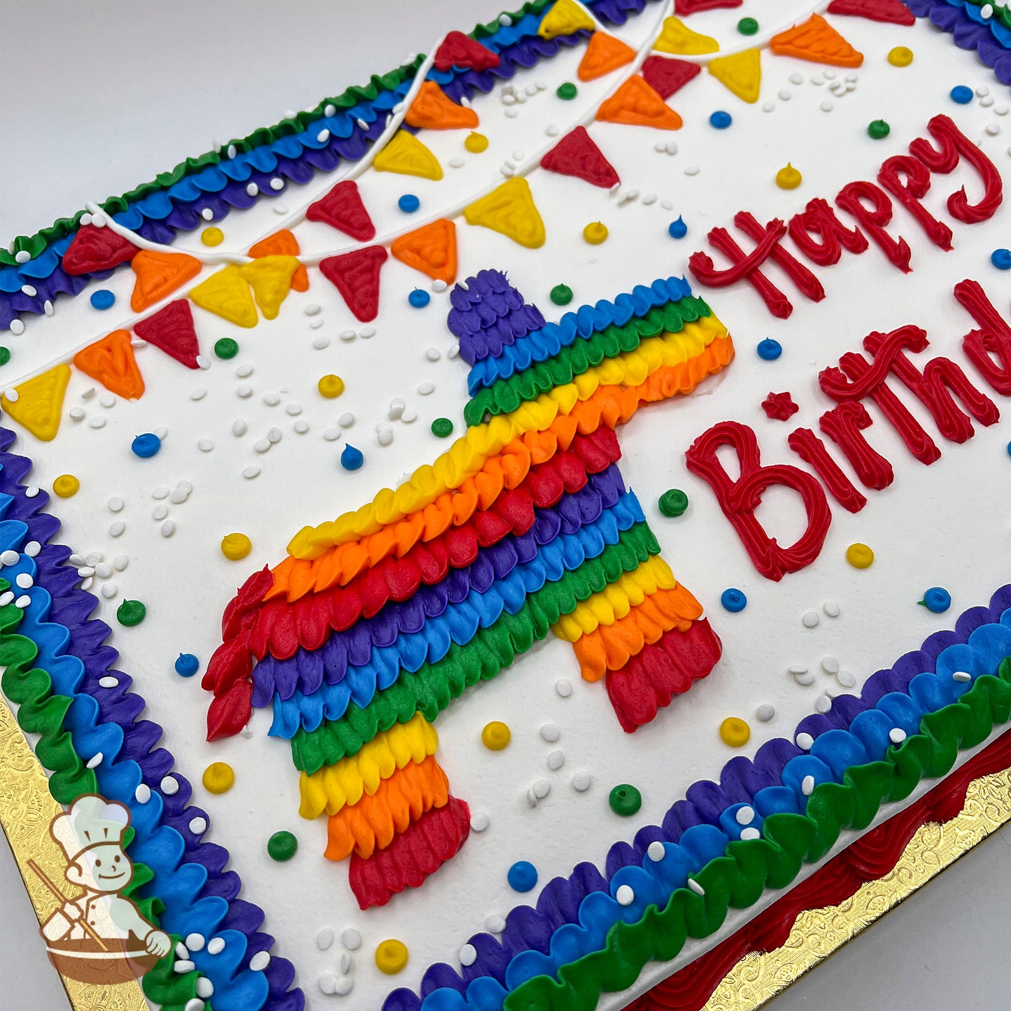 Sheet cake with a colorful buttercream piñata design, rainbow banner decorations, multicolored dots, and a piped border in purple, blue, and green.