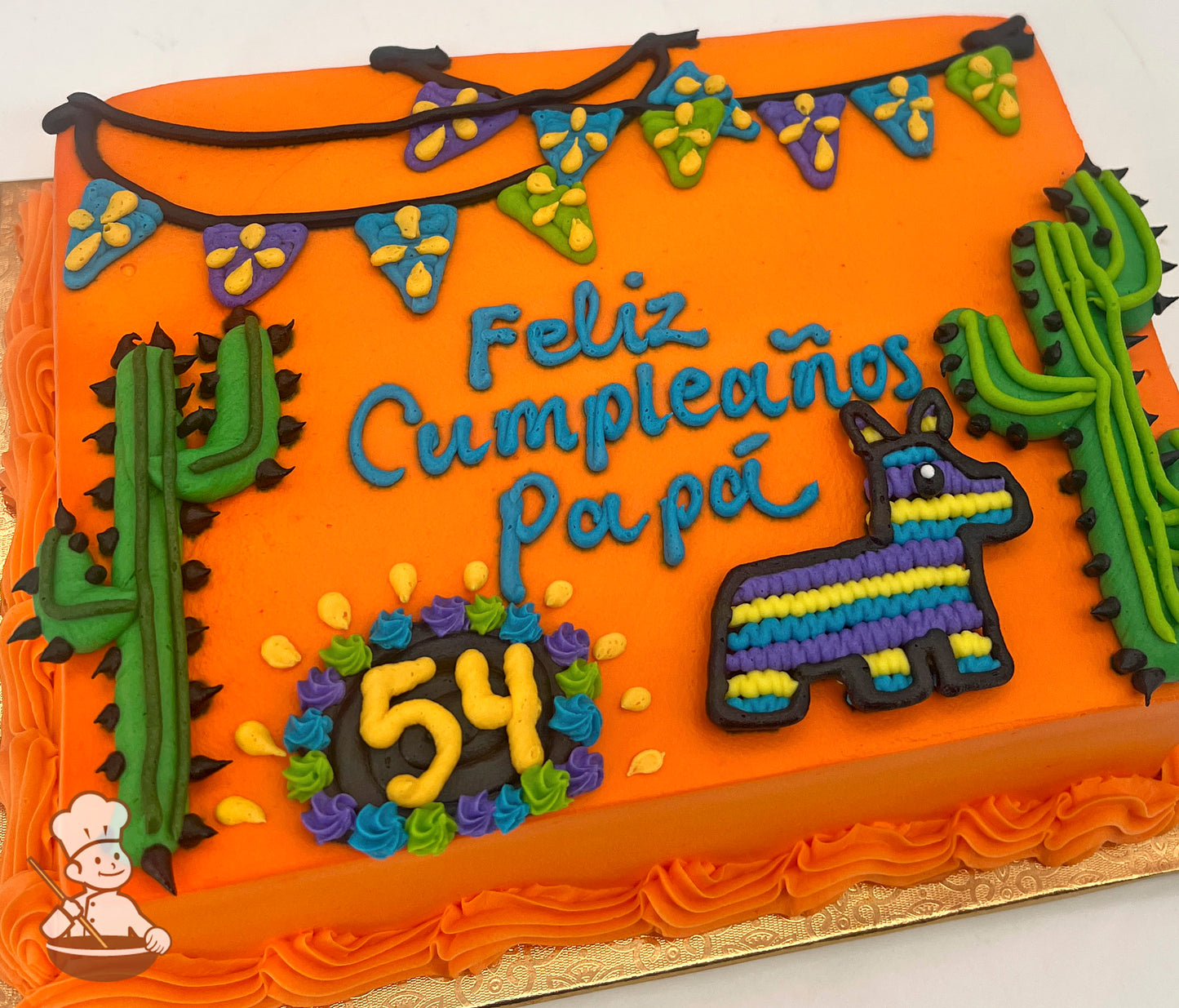 Orange sheet cake with buttercream decorations, including green cacti with black spines, a colorful striped piñata, a "54" in a floral wreath, and a banner with yellow and purple accents.