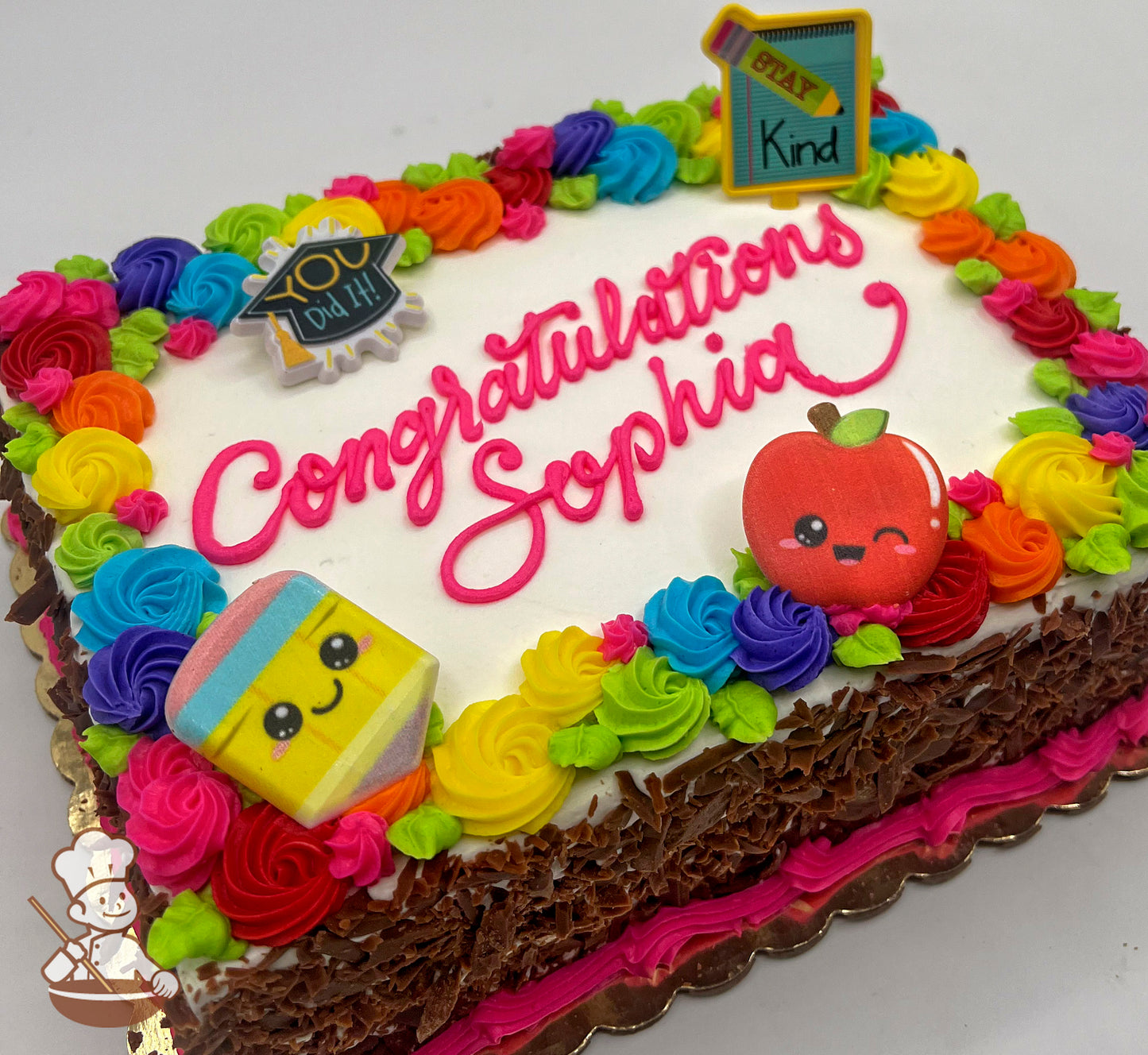 Sheet cake with colorful buttercream swirls in rainbow colors, plastic toppers of a smiling apple, pencil, and chalkboard.