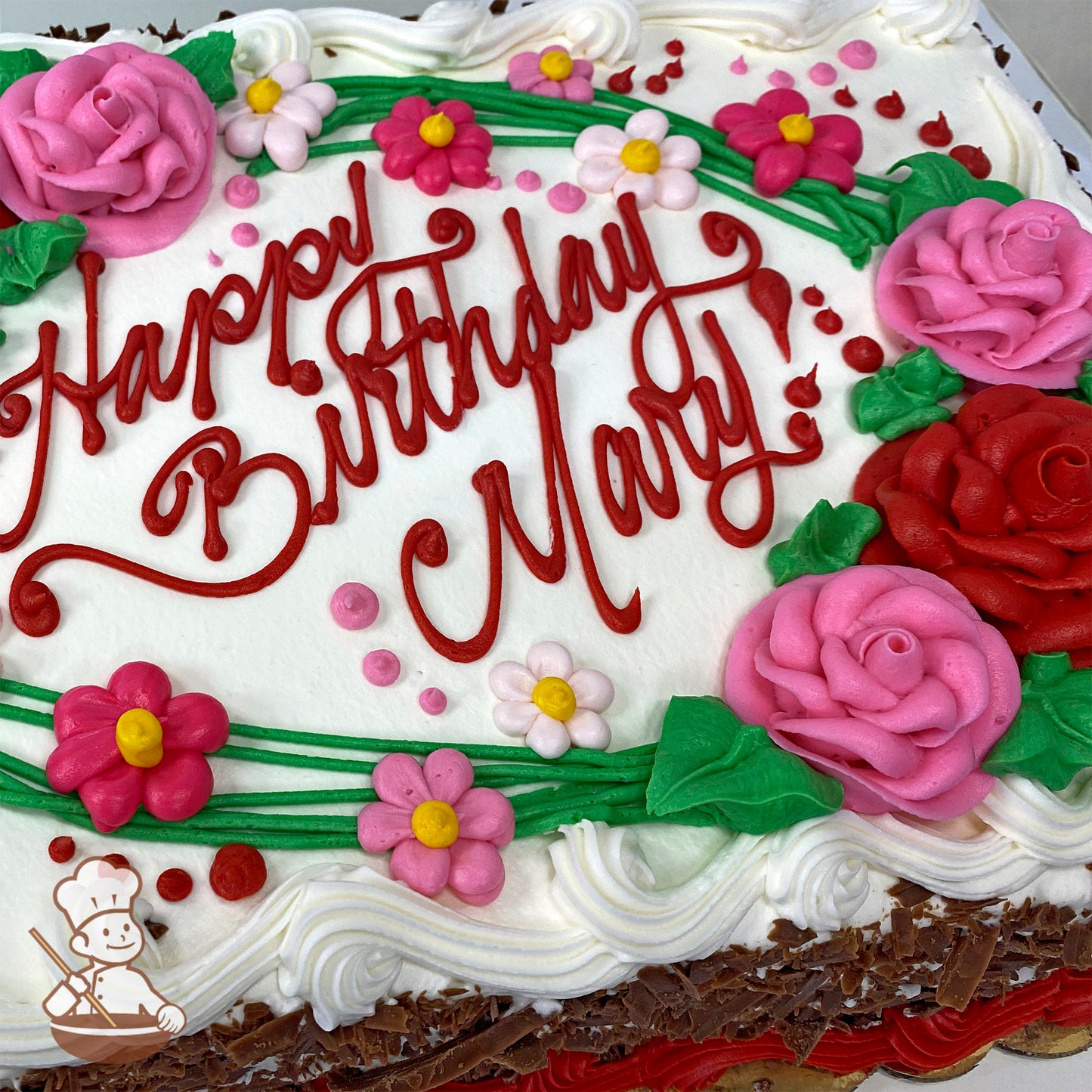 Sheet cake with buttercream decorations, featuring pink and red roses, pink daisies, green vines, leaves, and red dots on white frosting.