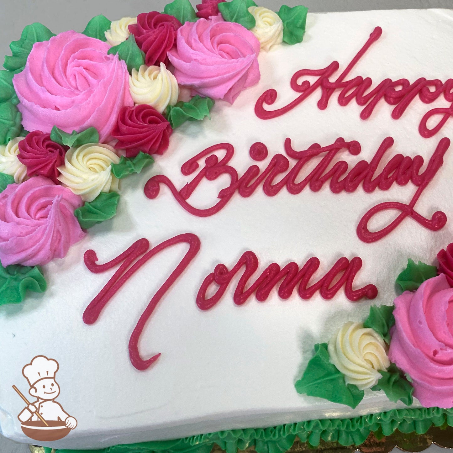Sheet cake with pink, red, and cream buttercream rosettes, green leaves, and piped border.