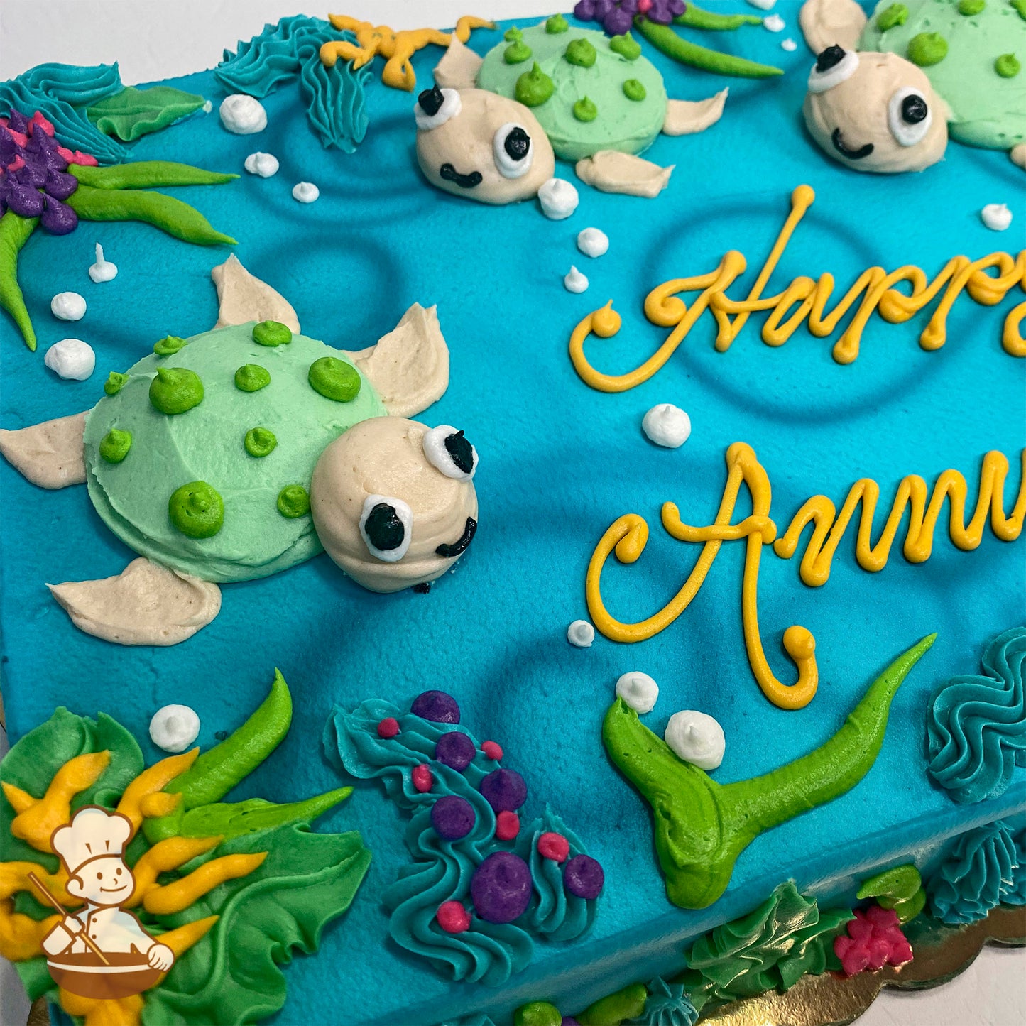 Sheet cake with blue frosting, decorated with green sea turtle designs, colorful coral, kelp, and white bubble accents.