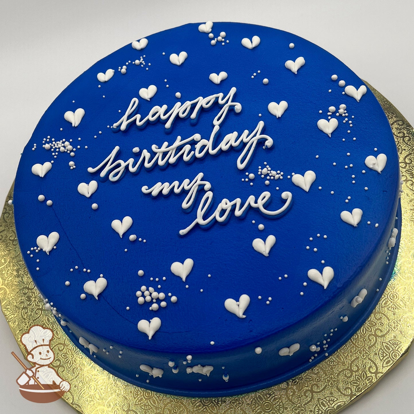 Round blue sheet cake with white buttercream hearts, sugar pearls, and a gold decorative base.