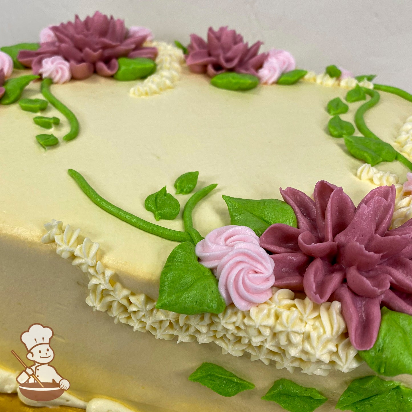 Sheet cake with buttercream decorations featuring mauve star-shaped flowers, pink rosettes, green vines, and leaves on a smooth cream-colored surface.