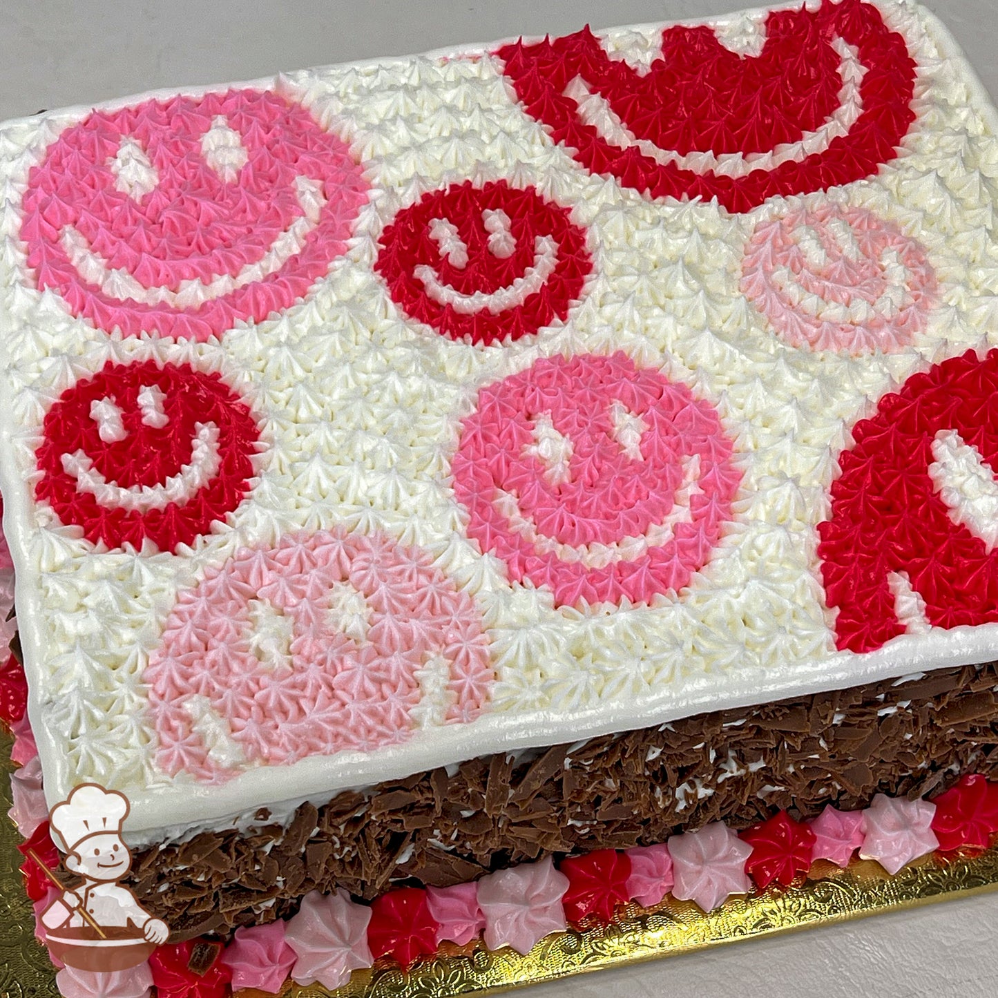 A sheet cake with white frosting, decorated with pink and red smiley faces made of piped star-shaped buttercream.
