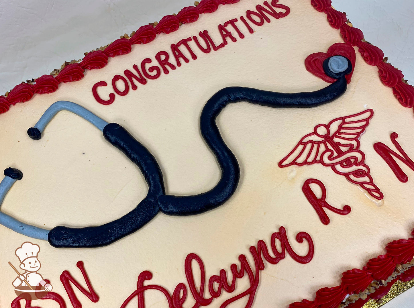Sheet cake with buttercream decorations, featuring a stethoscope design, RN symbol, and red piped borders.