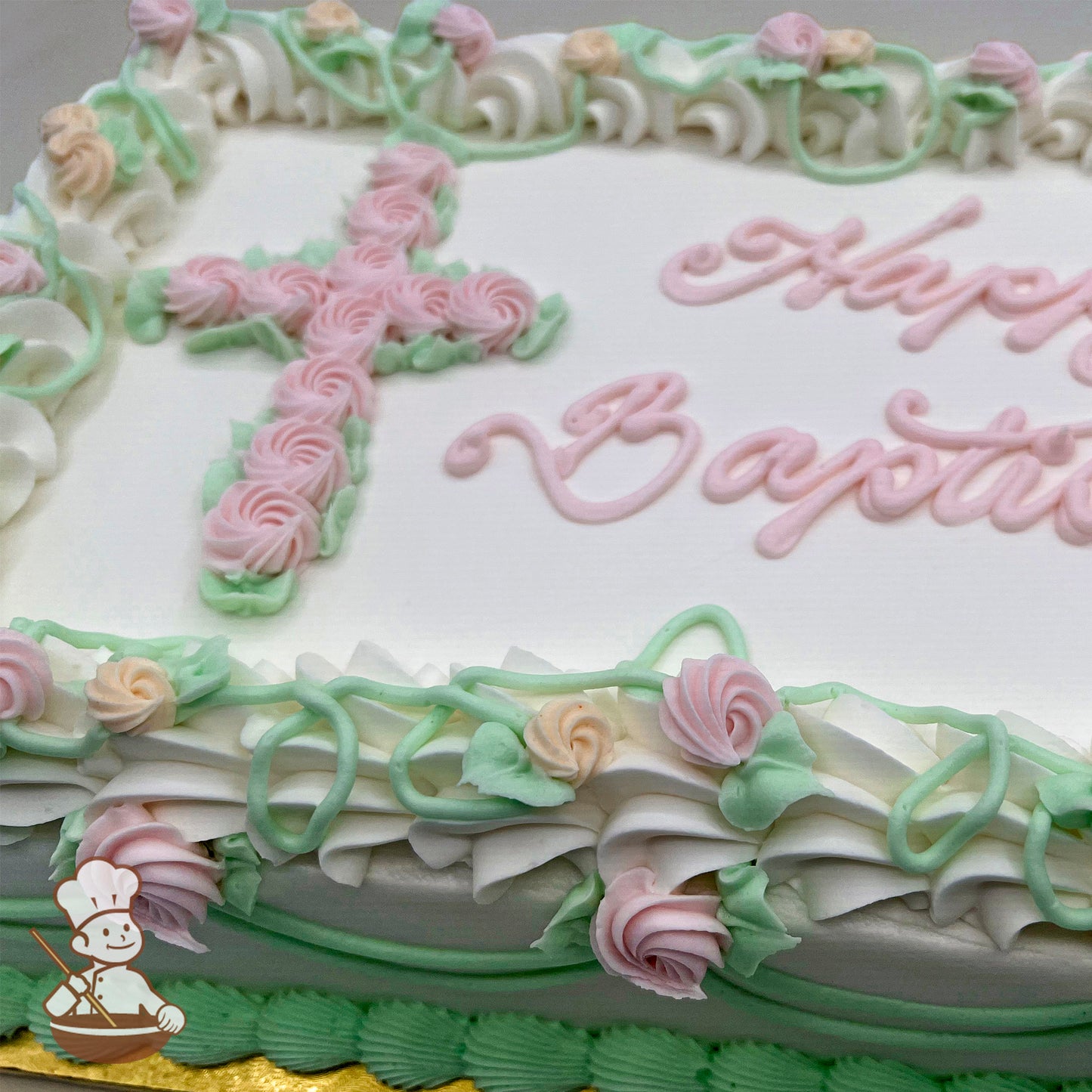 Sheet cake with white buttercream frosting, decorated with a pink buttercream cross made of rosettes, green vines, and pastel pink and peach buttercream flowers.