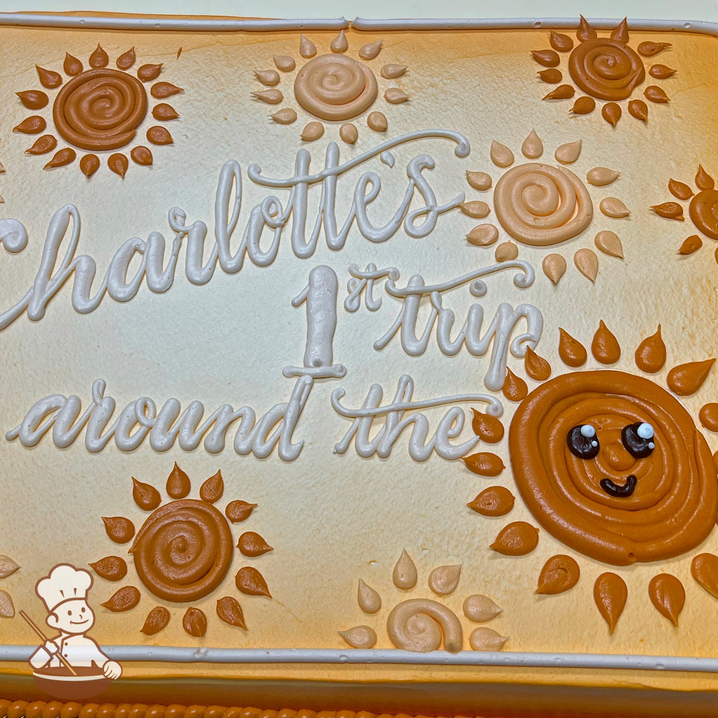 Sheet cake with buttercream decorations of swirled suns in orange and beige tones, featuring a smiling sun with a happy face in the bottom right corner.