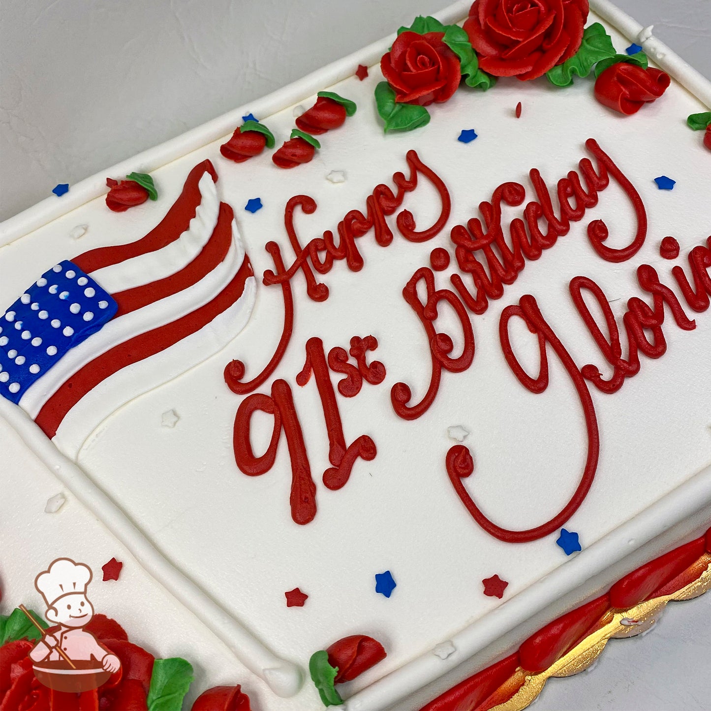 Sheet cake with white frosting, red buttercream roses, a USA flag design, and red, white, and blue star sprinkles.