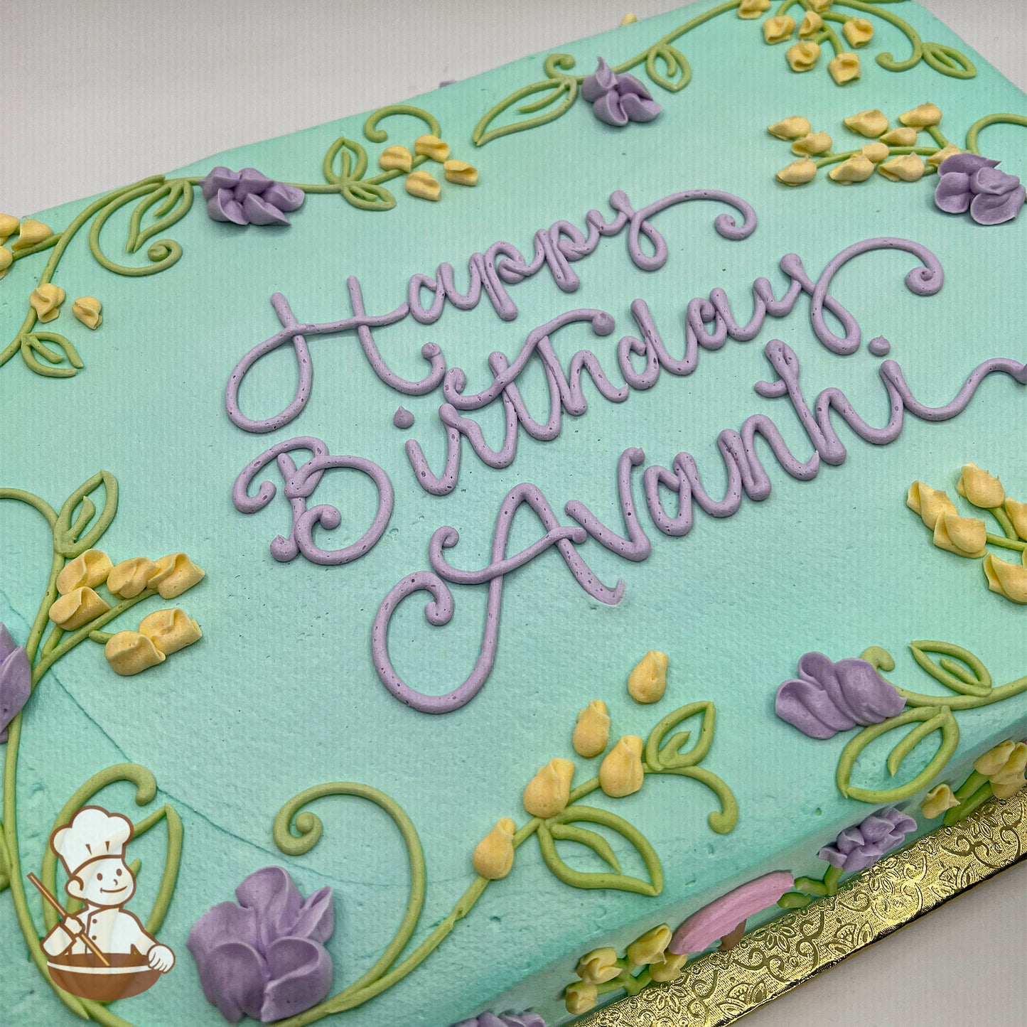 Light blue sheet cake with buttercream decorations of yellow and purple wildflowers, including sweet peas and buttercups, with green vine accents.
