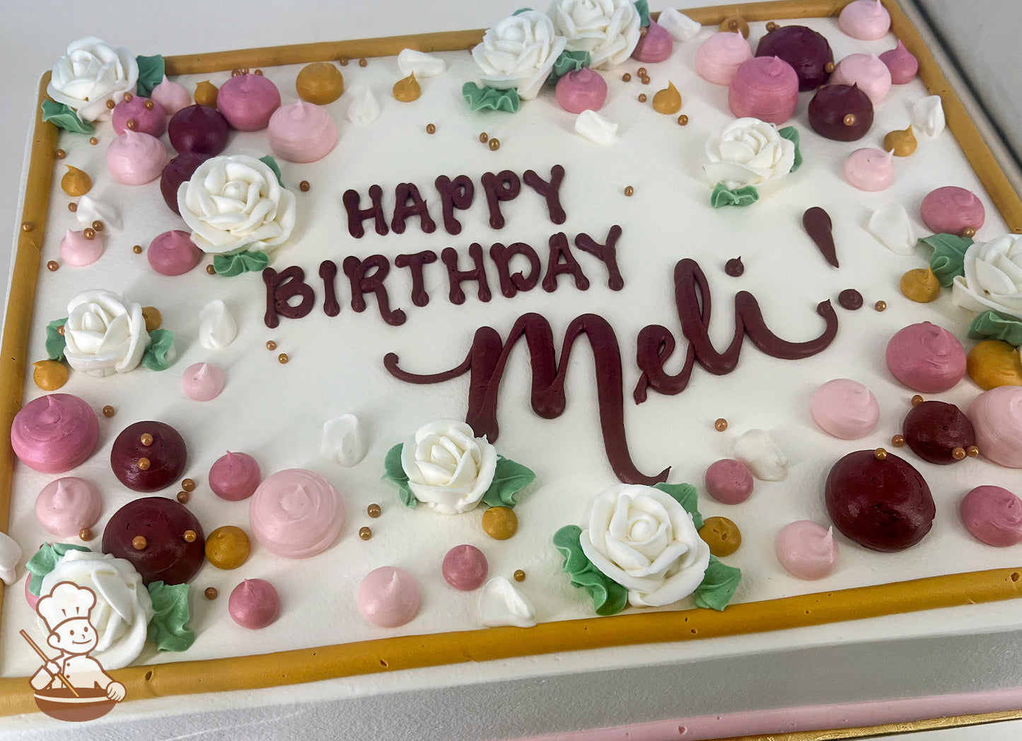 A sheet cake with white frosting, decorated with white buttercream roses, pink and burgundy dollops, gold pearl beads, and a gold border.