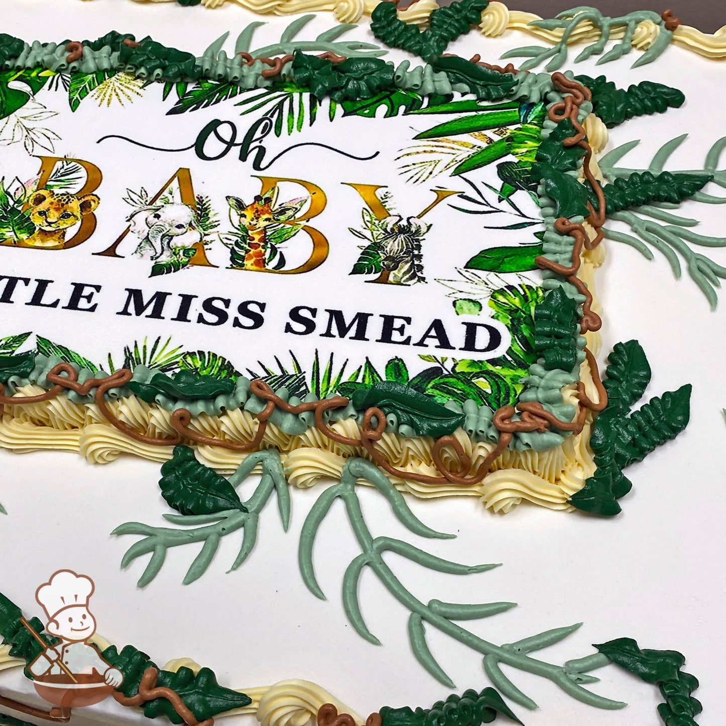 Sheet cake with buttercream decorations featuring green jungle leaves, vines, and brown branches surrounding a printed photo layer.